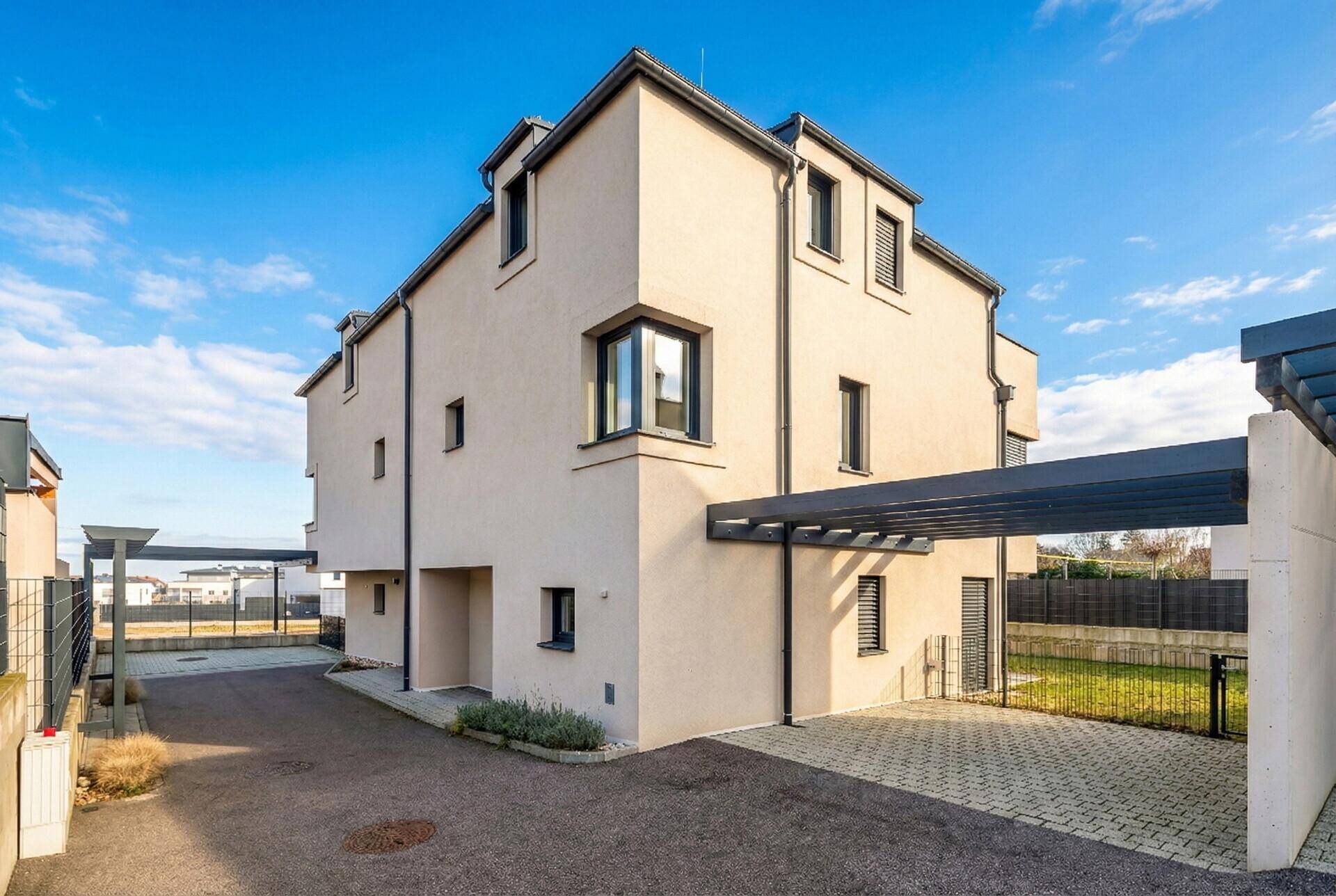 Moderne Reihenhausfassade mit Carport und gepflasterter Einfahrt.