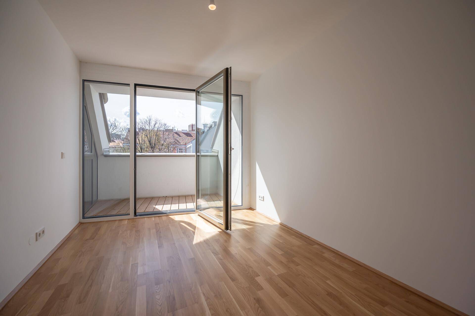Schlafzimmer mit Holzboden und Zugang zu einem kleinen Balkon, der viel Sonnenlicht bietet.