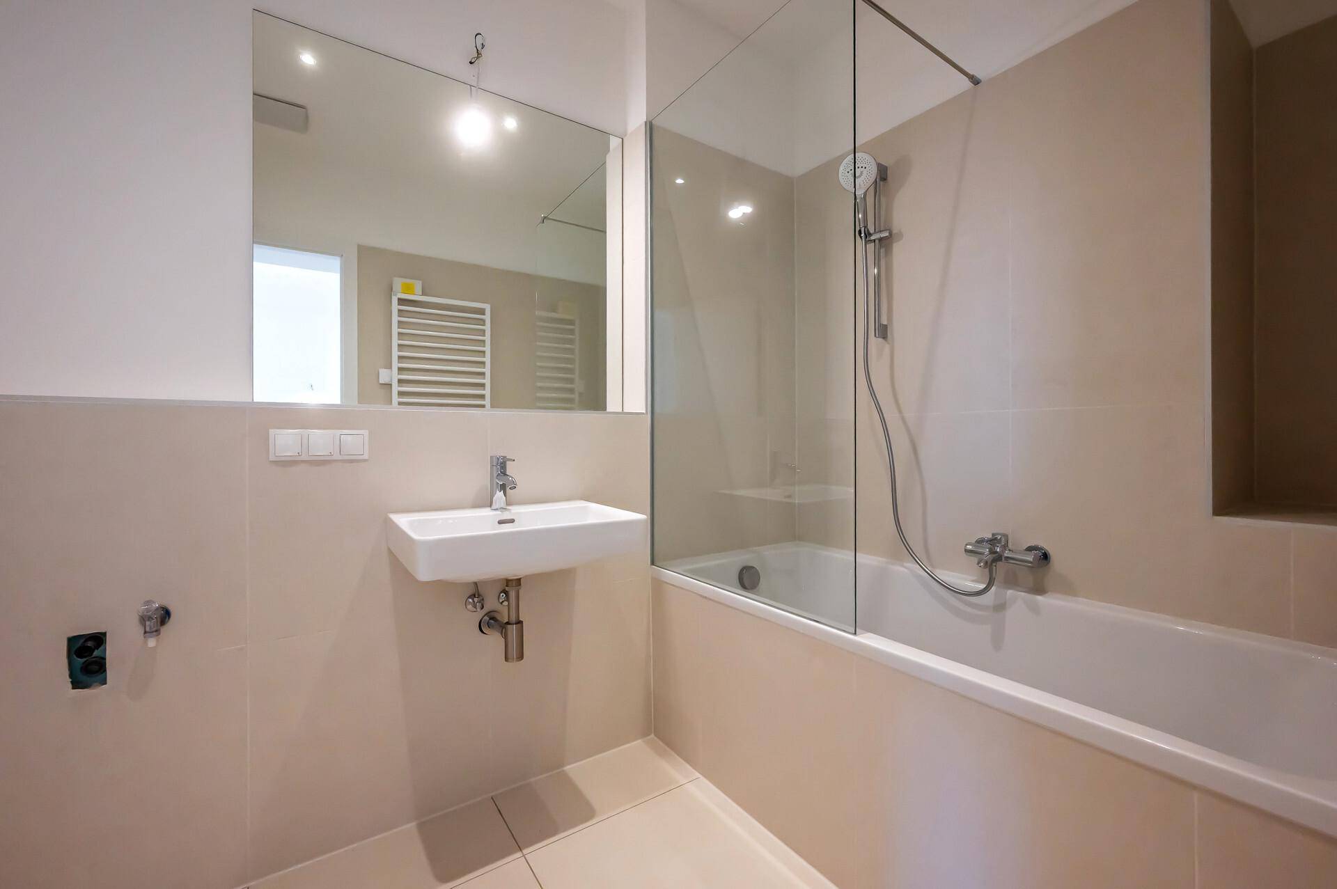 Modernes Badezimmer mit Badewanne, Glasduschwand, wandhängendem Waschbecken und großem Spiegel.