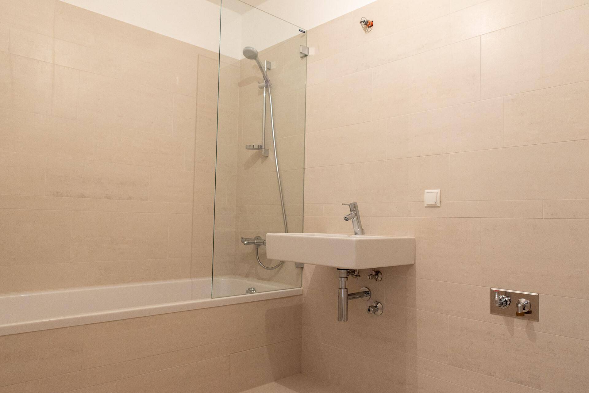 Helles Badezimmer mit Badewanne, Duschfunktion und modernem Waschbecken, komplett gefliest.