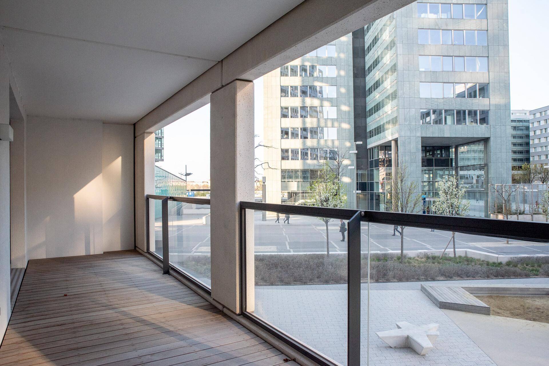 Geräumiger Balkon mit Holzboden und Glasgeländer, bietet einen weiten Blick auf die Stadt.