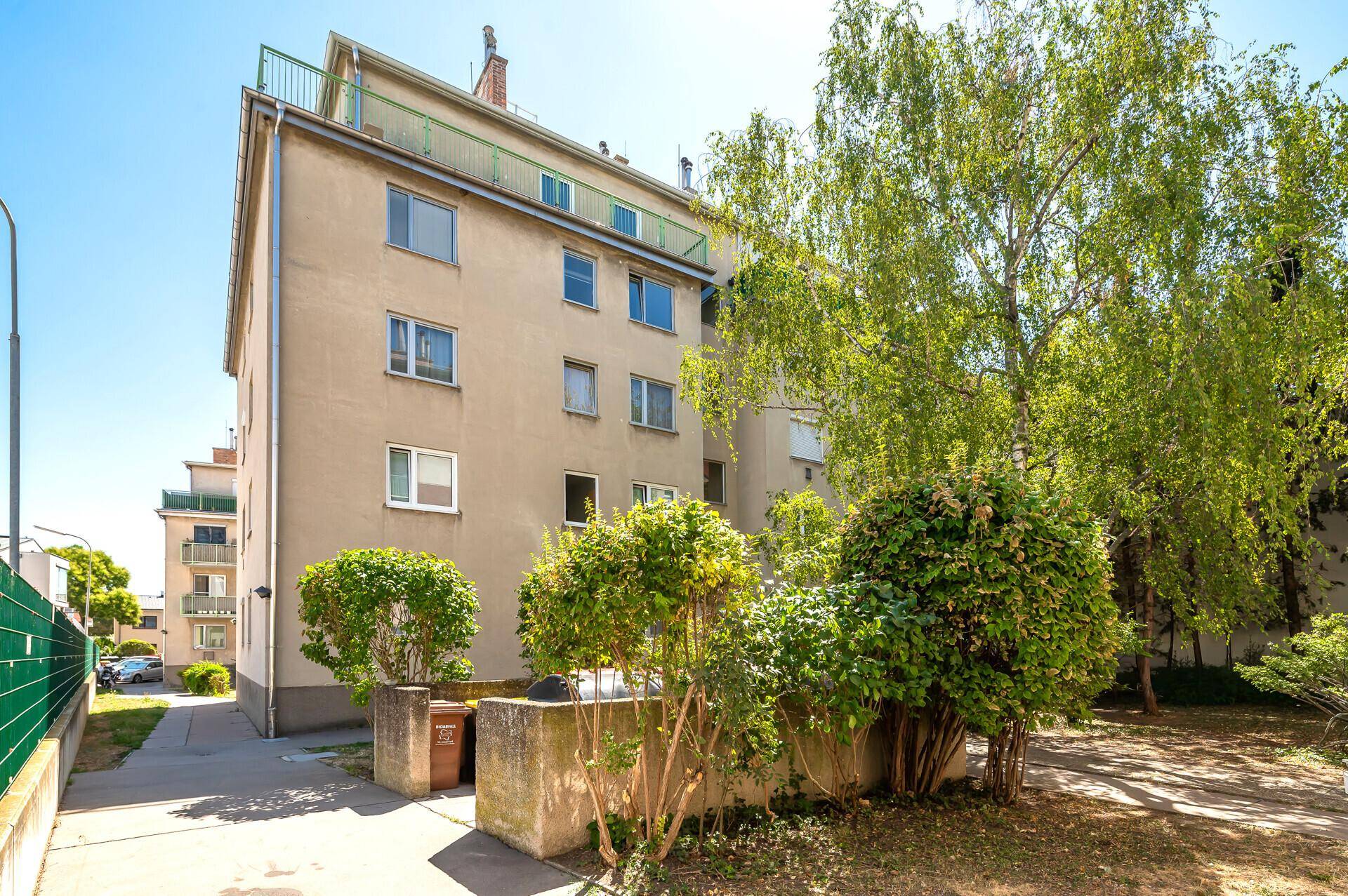 Seitenansicht eines Mehrfamilienhauses mit Bäumen und Grünflächen.