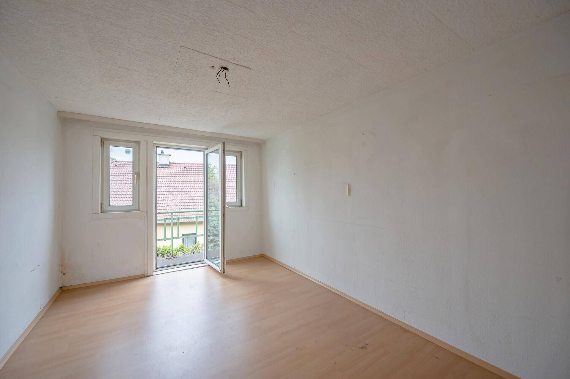 Helles Zimmer mit Holzboden und Zugang zu einem kleinen Balkon.