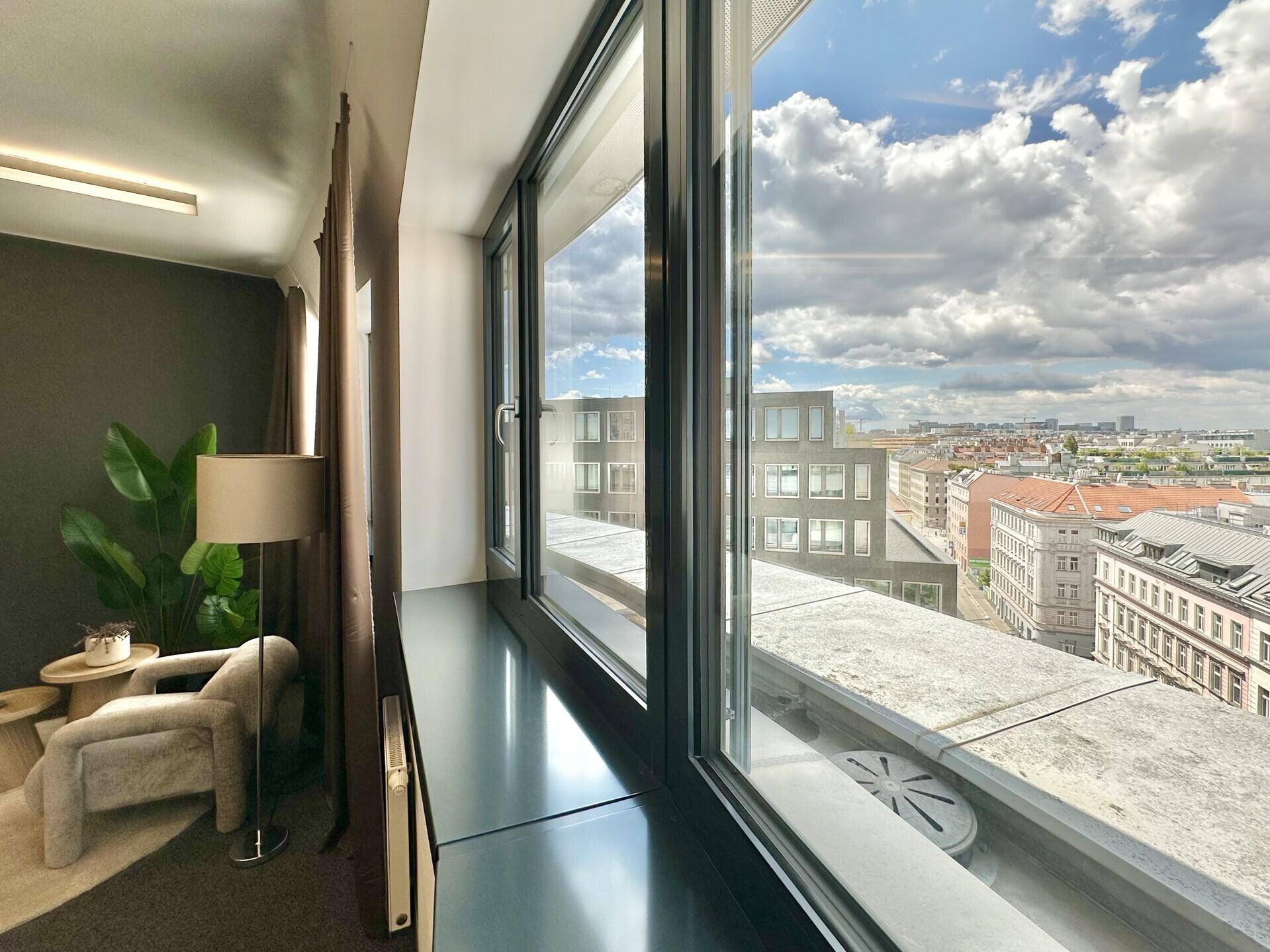 Innenraum mit großen Fenstern, die einen weiten Blick über die Stadt und den Himmel bieten.