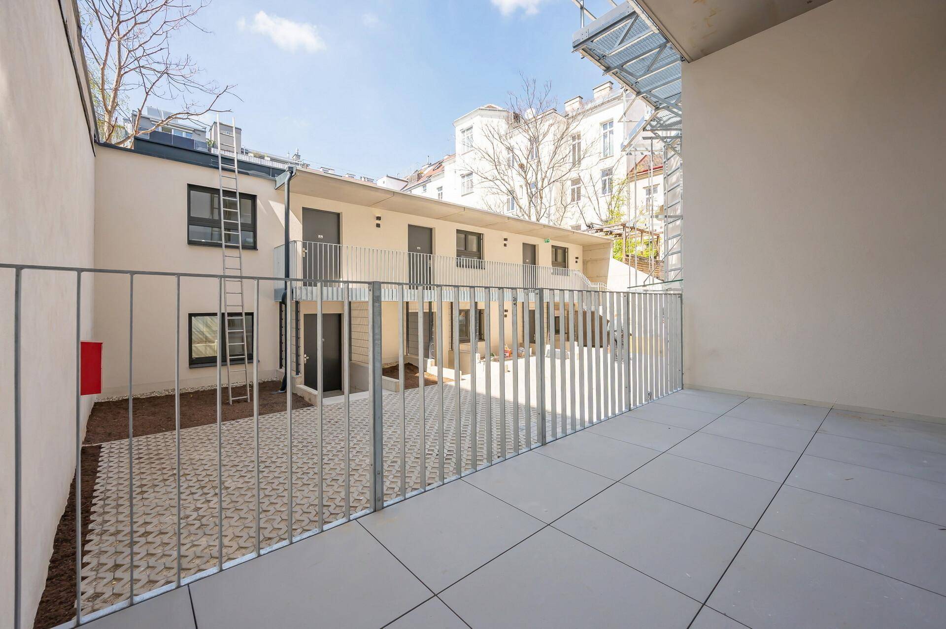 Große, gepflasterte Terrasse mit Metallgeländer und Blick auf den Innenhof und angrenzende Gebäude.