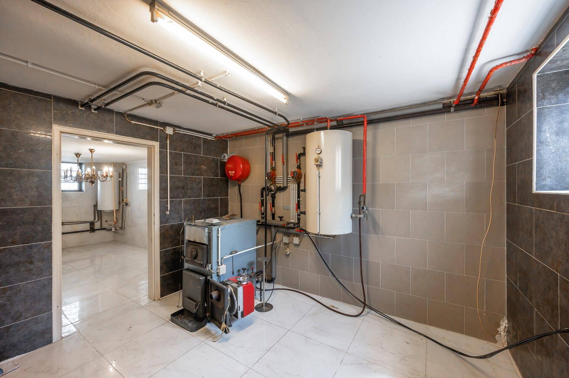 Heizungsraum im Keller mit Kessel, Warmwasserspeicher und sichtbaren Rohren.