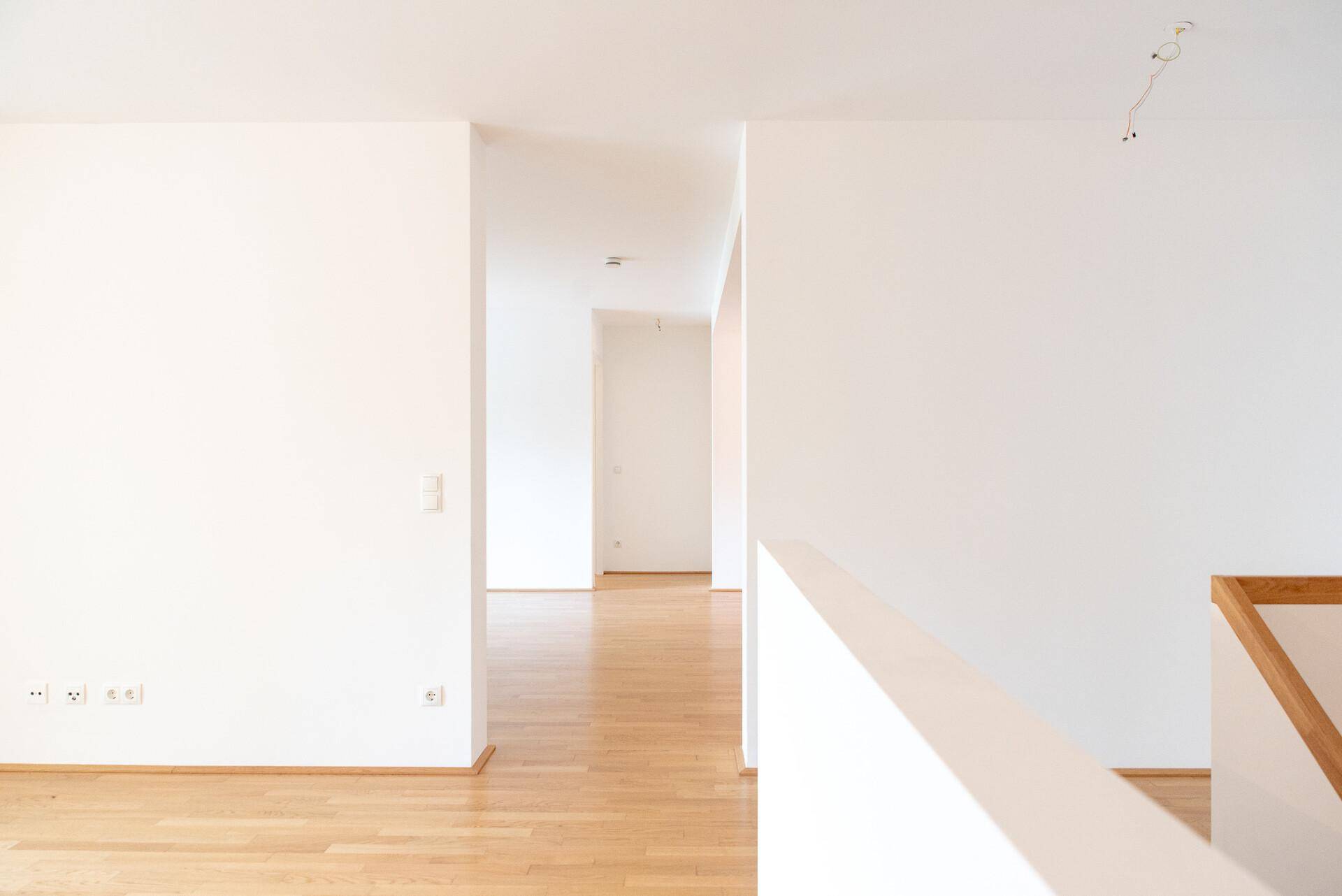 Langer, heller Flur mit Holzboden und weiß gestrichenen Wänden, der zu weiteren Räumen führt.