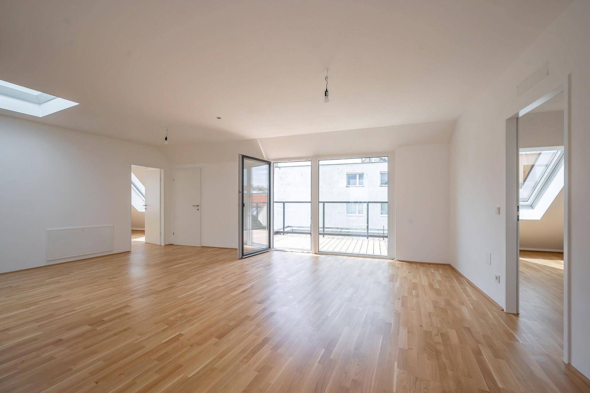 Geräumiger, heller Wohnbereich mit Holzparkett, Dachfenster und französischem Balkon.