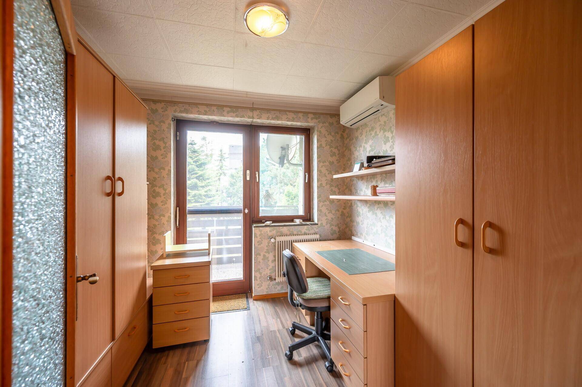 Helles Arbeitszimmer mit Schreibtisch, Schränken und direktem Zugang zum Balkon.