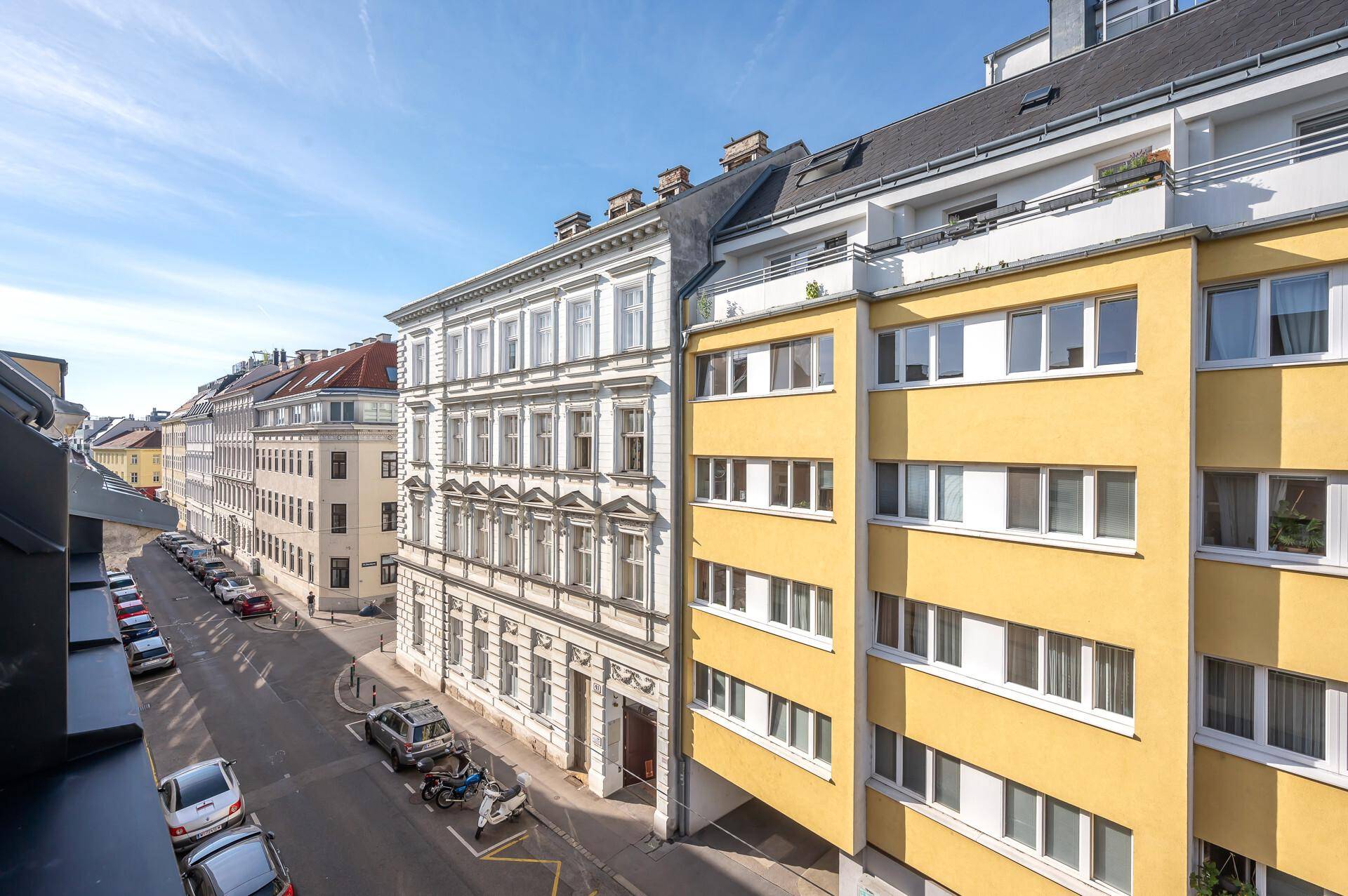 Blick von oben auf eine belebte Stadtstraße mit historischen und modernen Gebäuden.