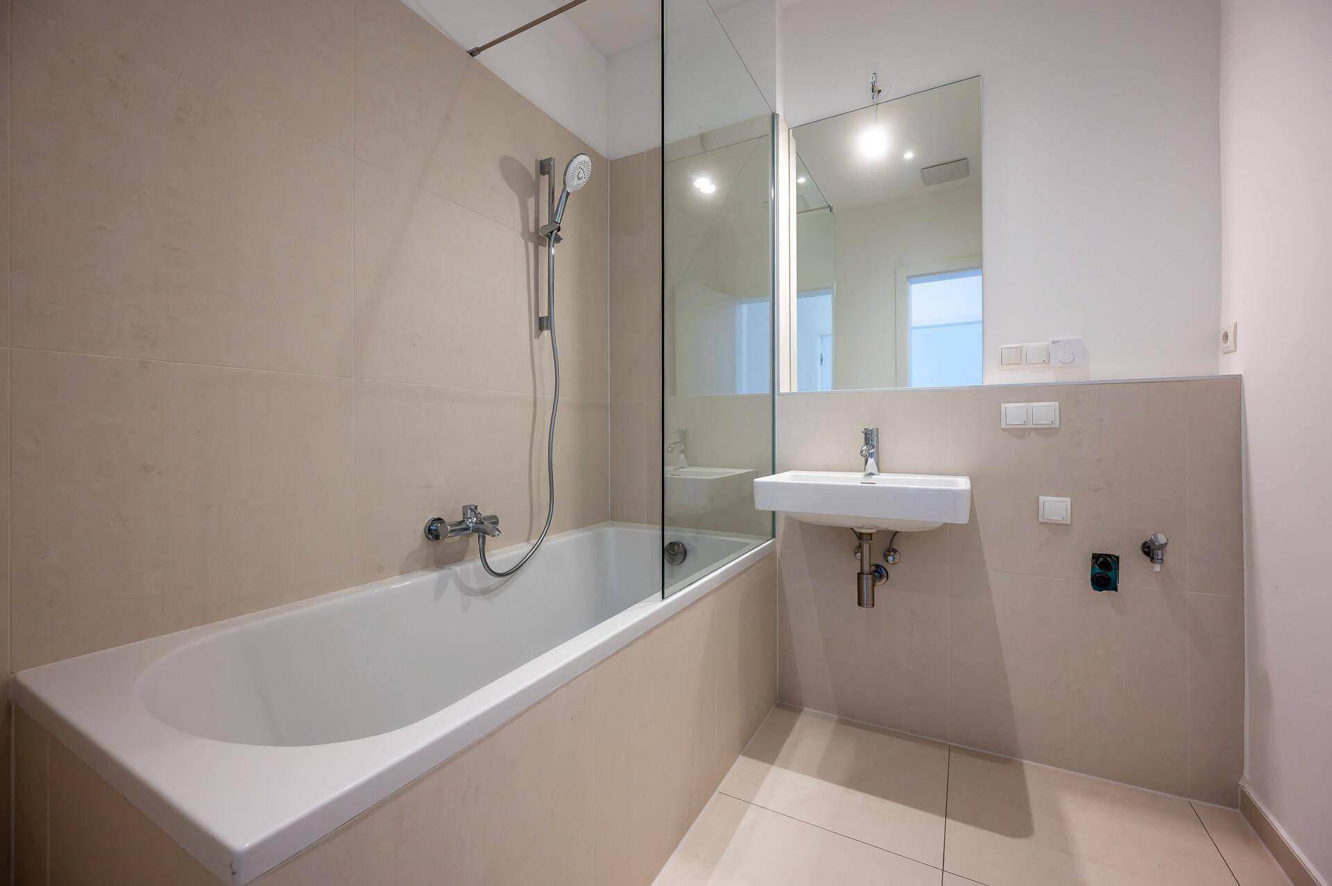 Modernes Badezimmer mit Badewanne, Glasduschwand, wandmontiertem Waschbecken und beigefarbenen Fliesen.