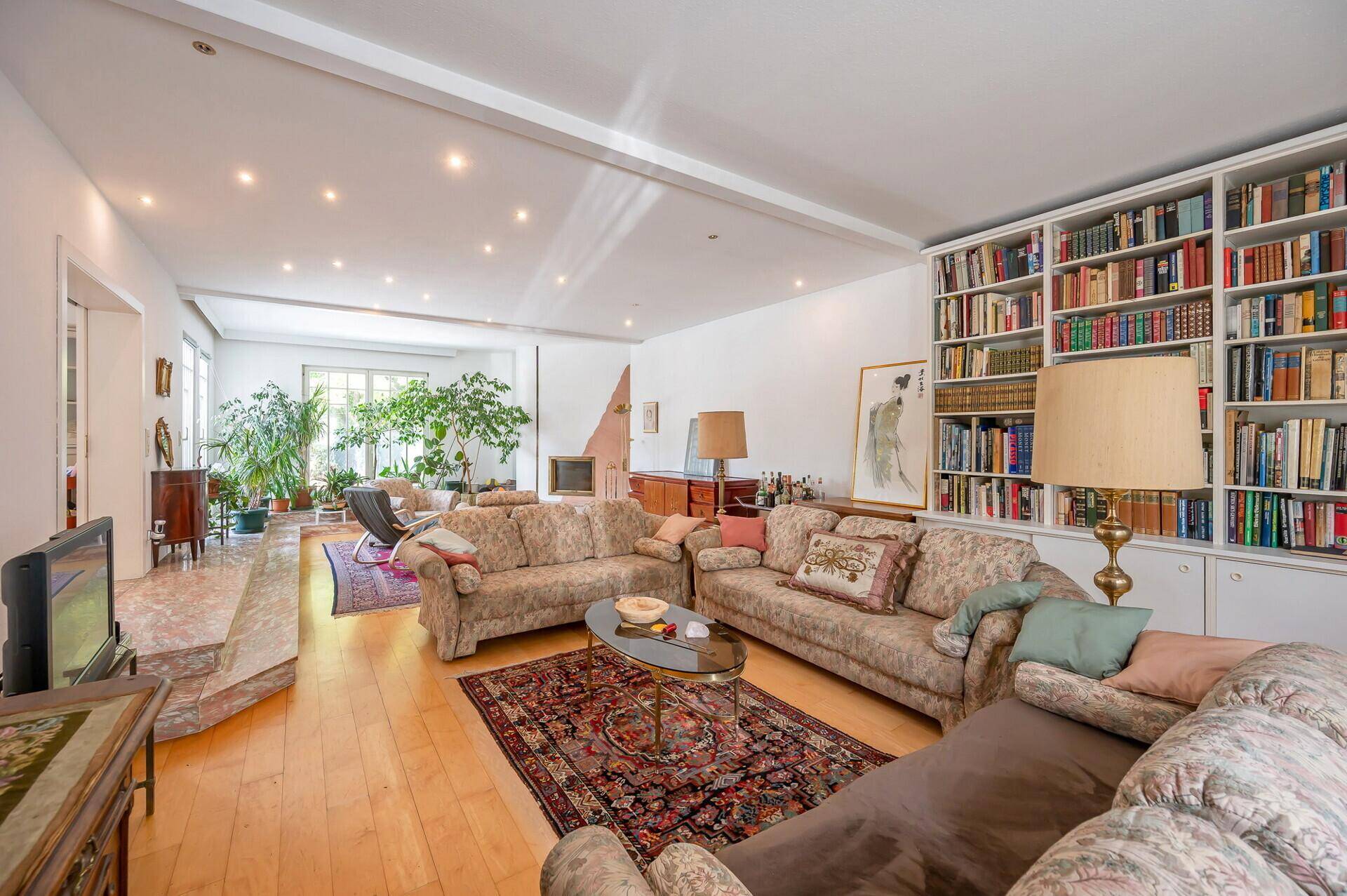 Weitläufiges Wohnzimmer mit Bücherregal, bequemen Sofas und Parkettboden.