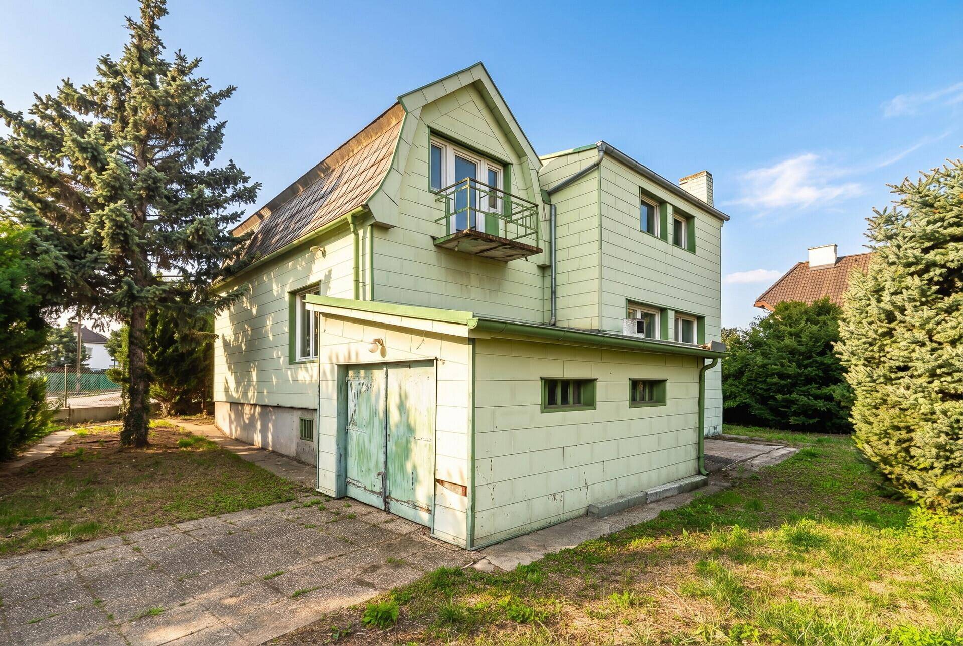 Seitenansicht des grünen Einfamilienhauses mit Garage und kleinem Balkon im Obergeschoss.