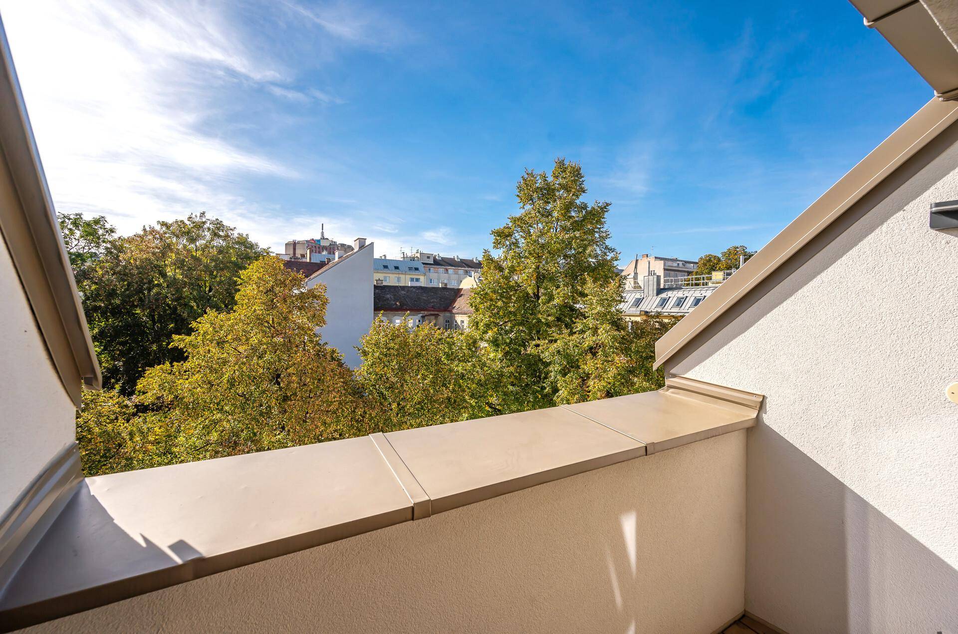 Kleiner Balkon mit Blick auf grüne Bäume und die Dächer der Stadt.