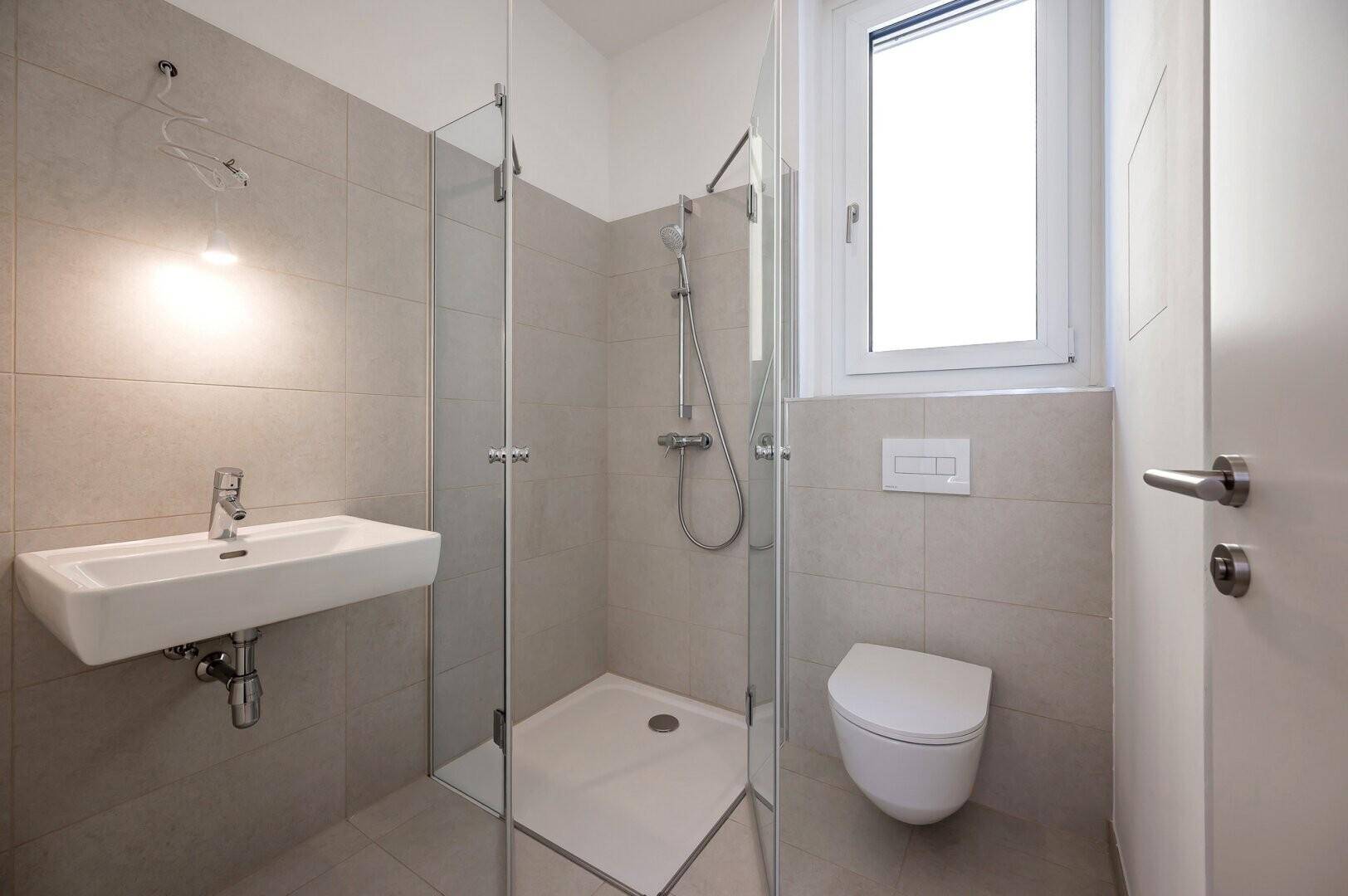 Modernes Badezimmer mit Duschkabine, Waschbecken und wandhängendem WC, hell gefliest.