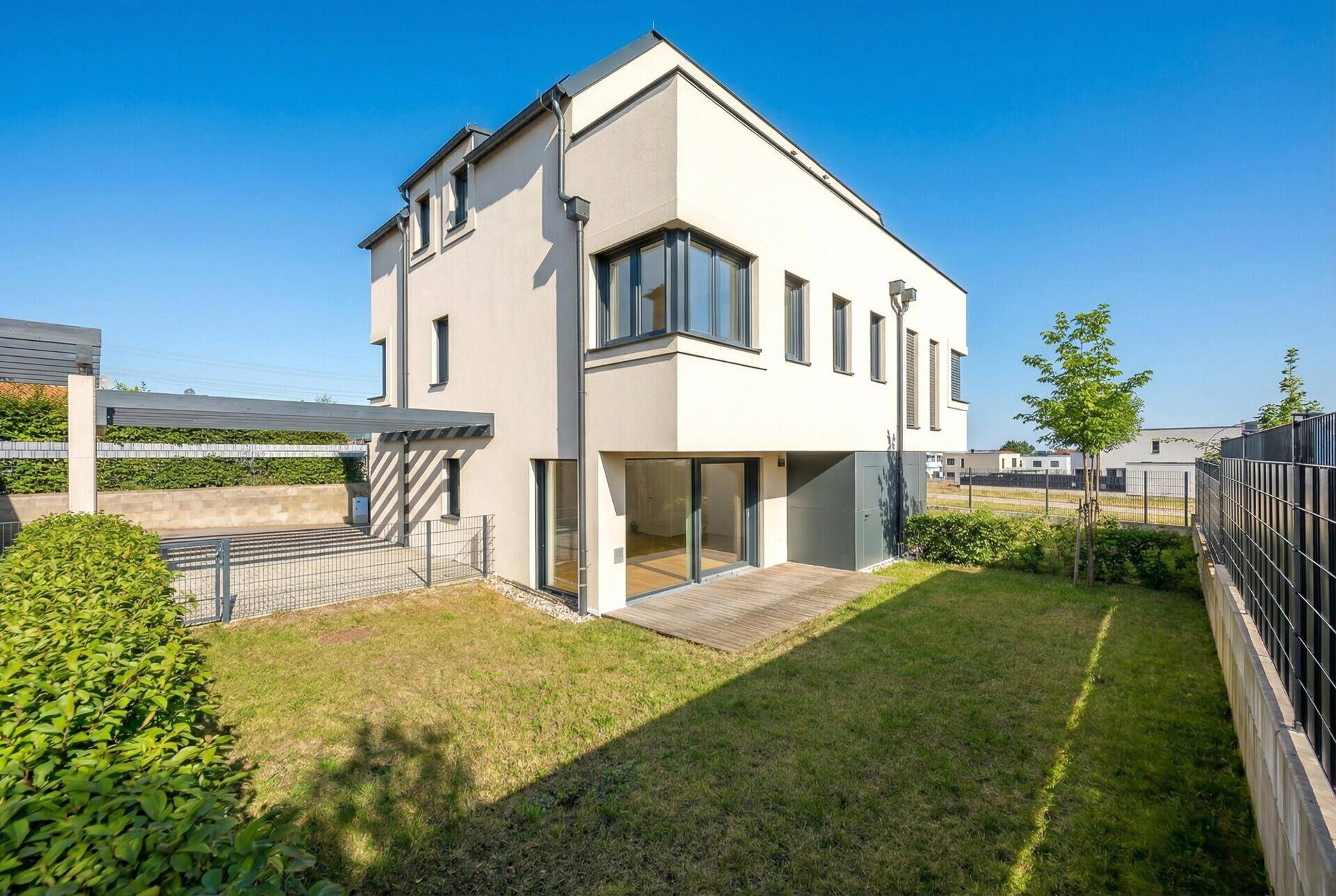 Moderne Hausfassade mit großem Garten und Holzterrasse.