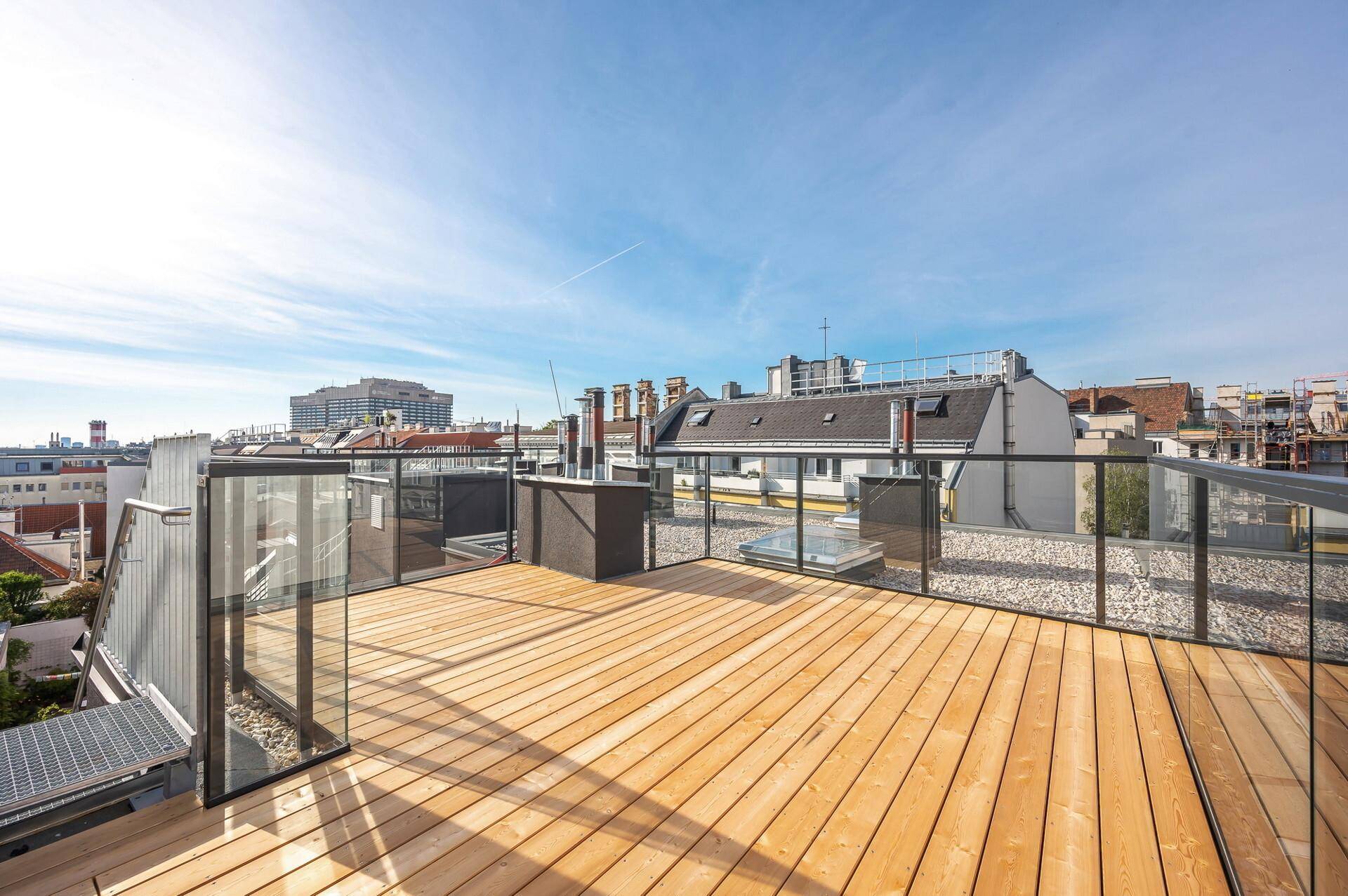 Geräumige Dachterrasse mit Holzboden und Glasgeländer, ideal für Entspannung im Freien.