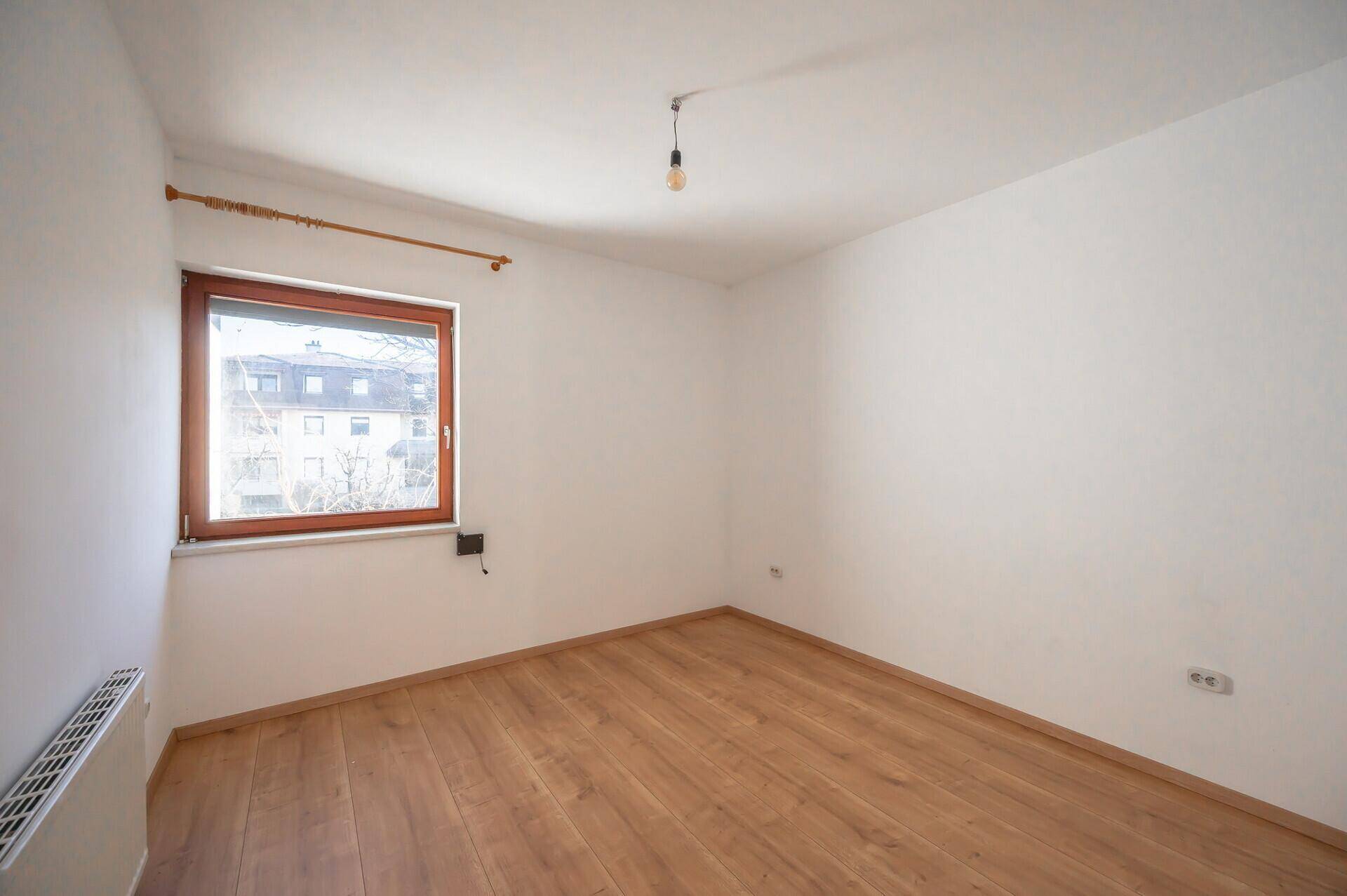 Geräumiges Schlafzimmer mit Holzboden, weißen Wänden und einem großen Fenster.