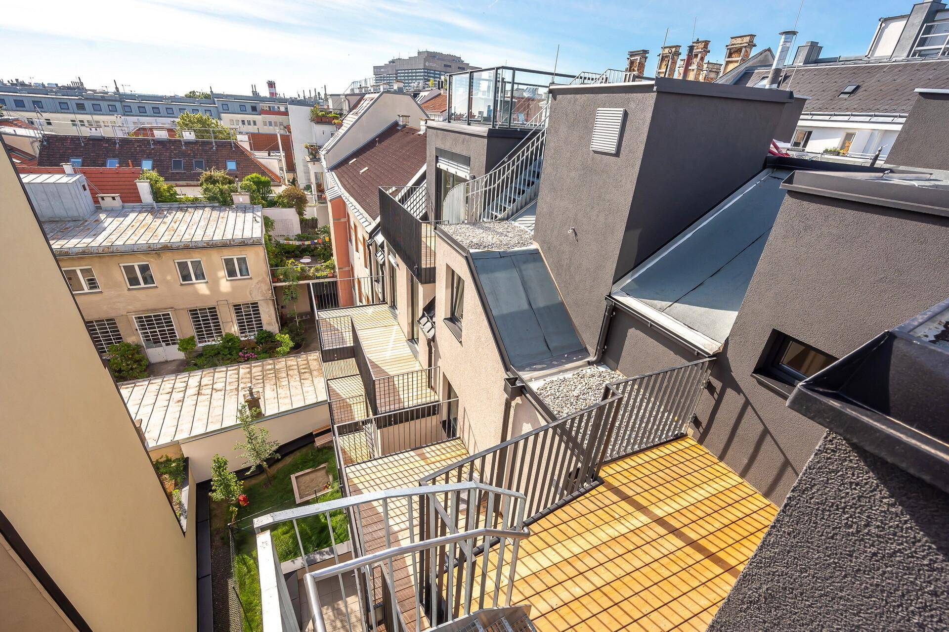 Mehrere Terrassen und Balkone mit Holzbelag und Metallgeländern in einer städtischen Umgebung.