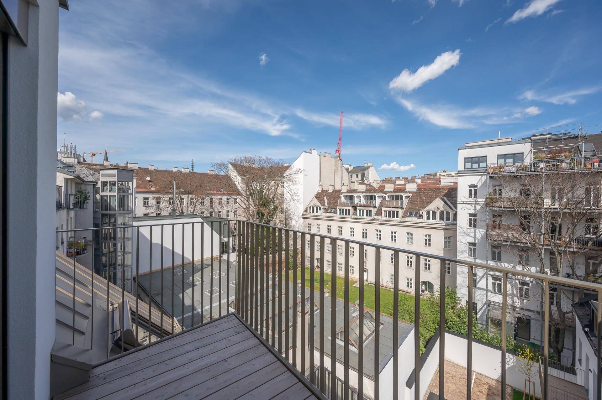 Balkon mit Metallgeländer und Blick auf einen begrünten Innenhof und umliegende Gebäude.