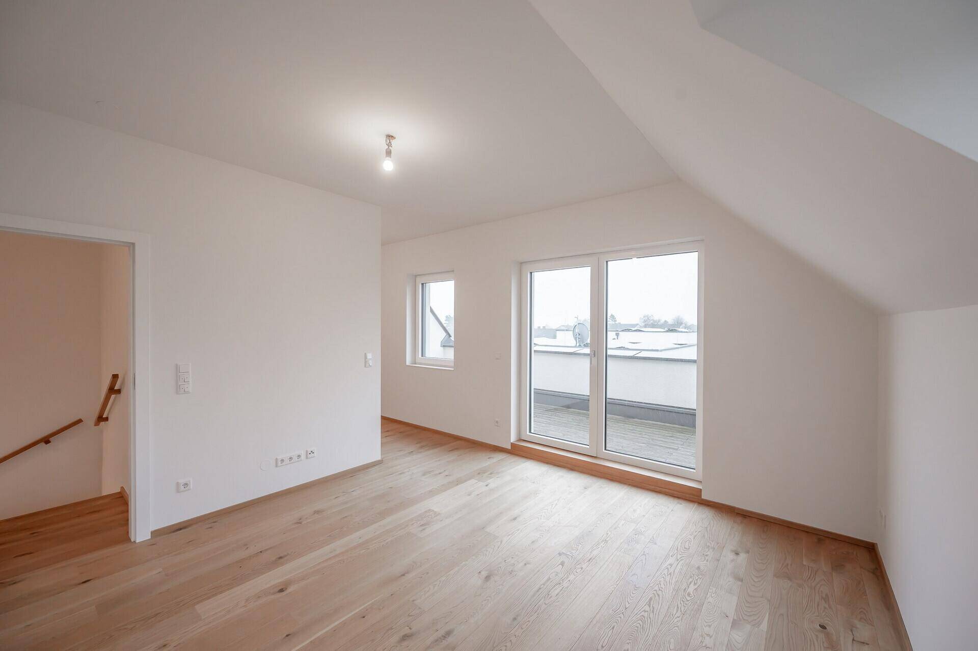 Helles Schlafzimmer im Dachgeschoss mit Holzboden und Zugang zur Dachterrasse.