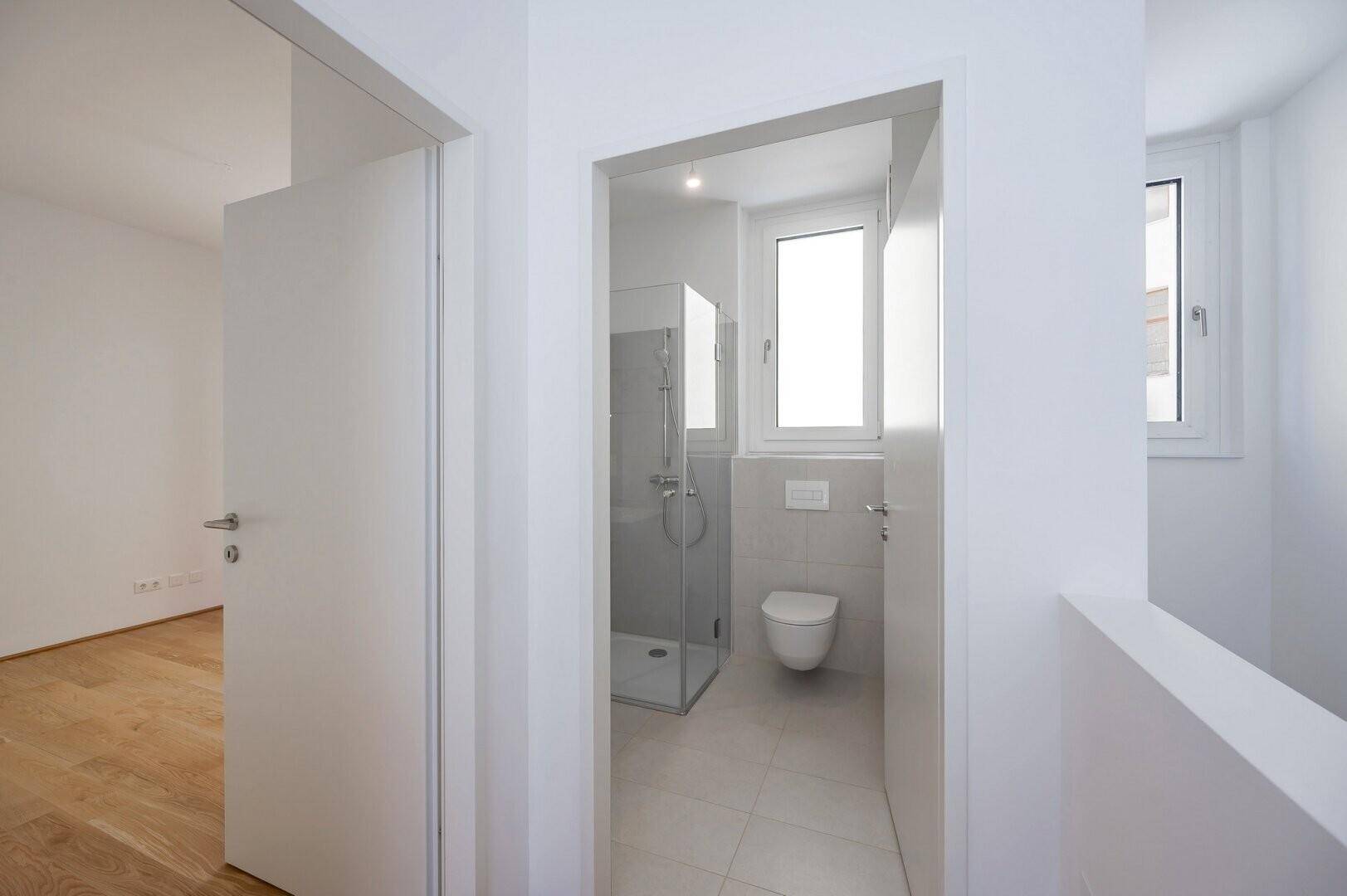 Moderner Badezimmerzugang mit Duschbereich und WC, hell gefliest.