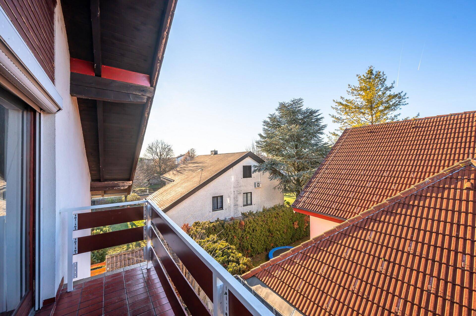 Balkon mit Blick auf die umliegenden Dächer und grüne Bäume an einem sonnigen Tag.