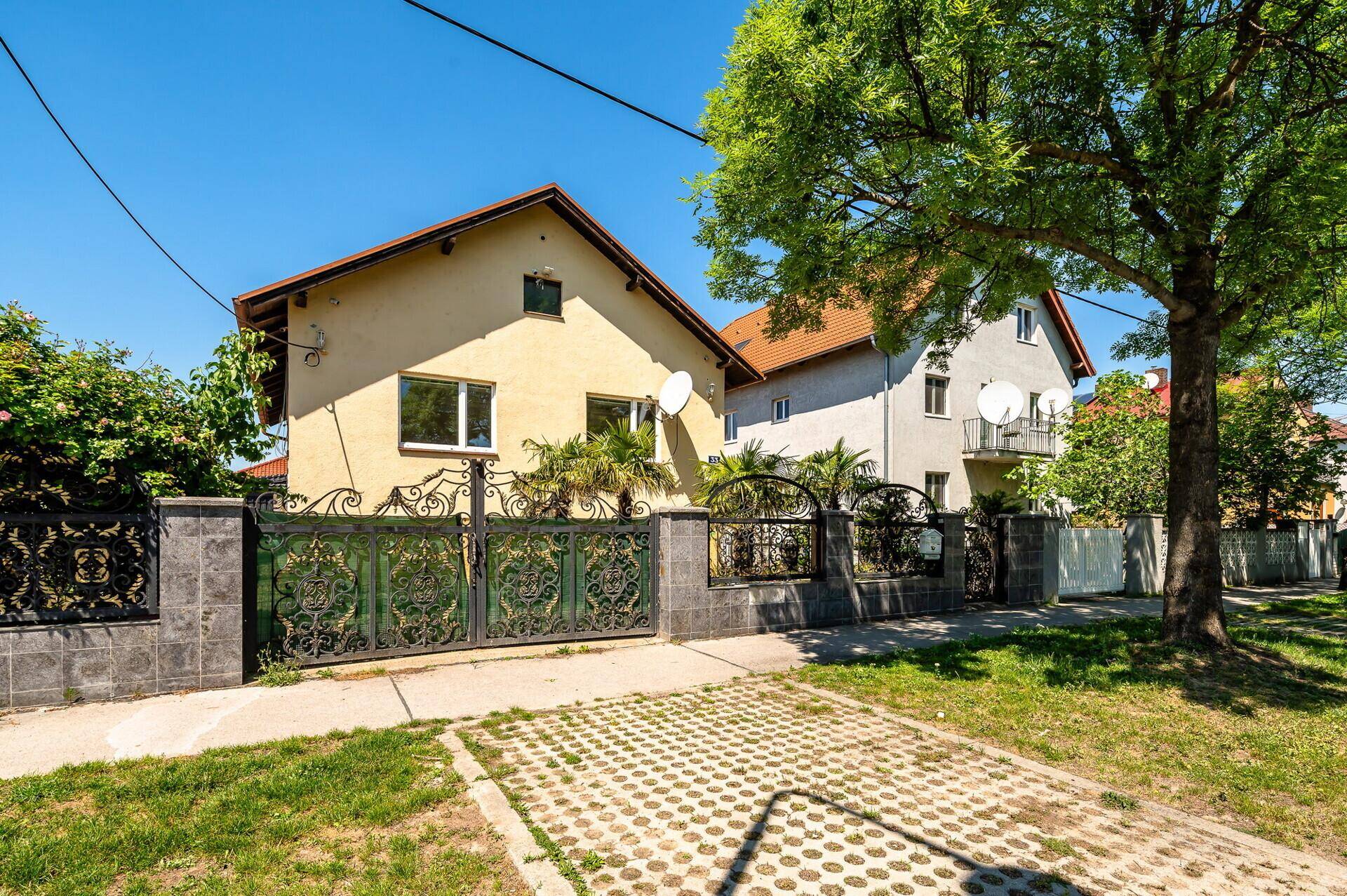 Ansicht des Hauses von der Straße mit schmiedeeisernem Zaun und gepflasterter Einfahrt.