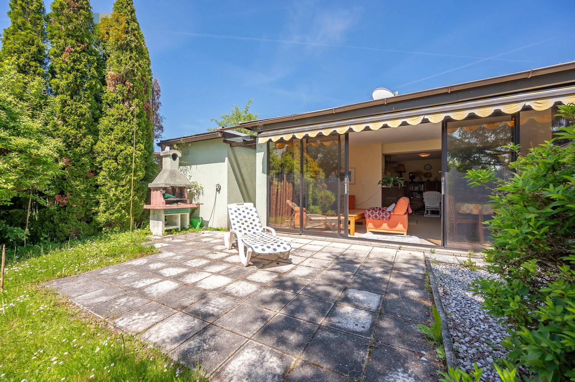 Terrasse mit Sonnenliege und Grillplatz, direkt vor den großen Glasschiebetüren des Hauses.