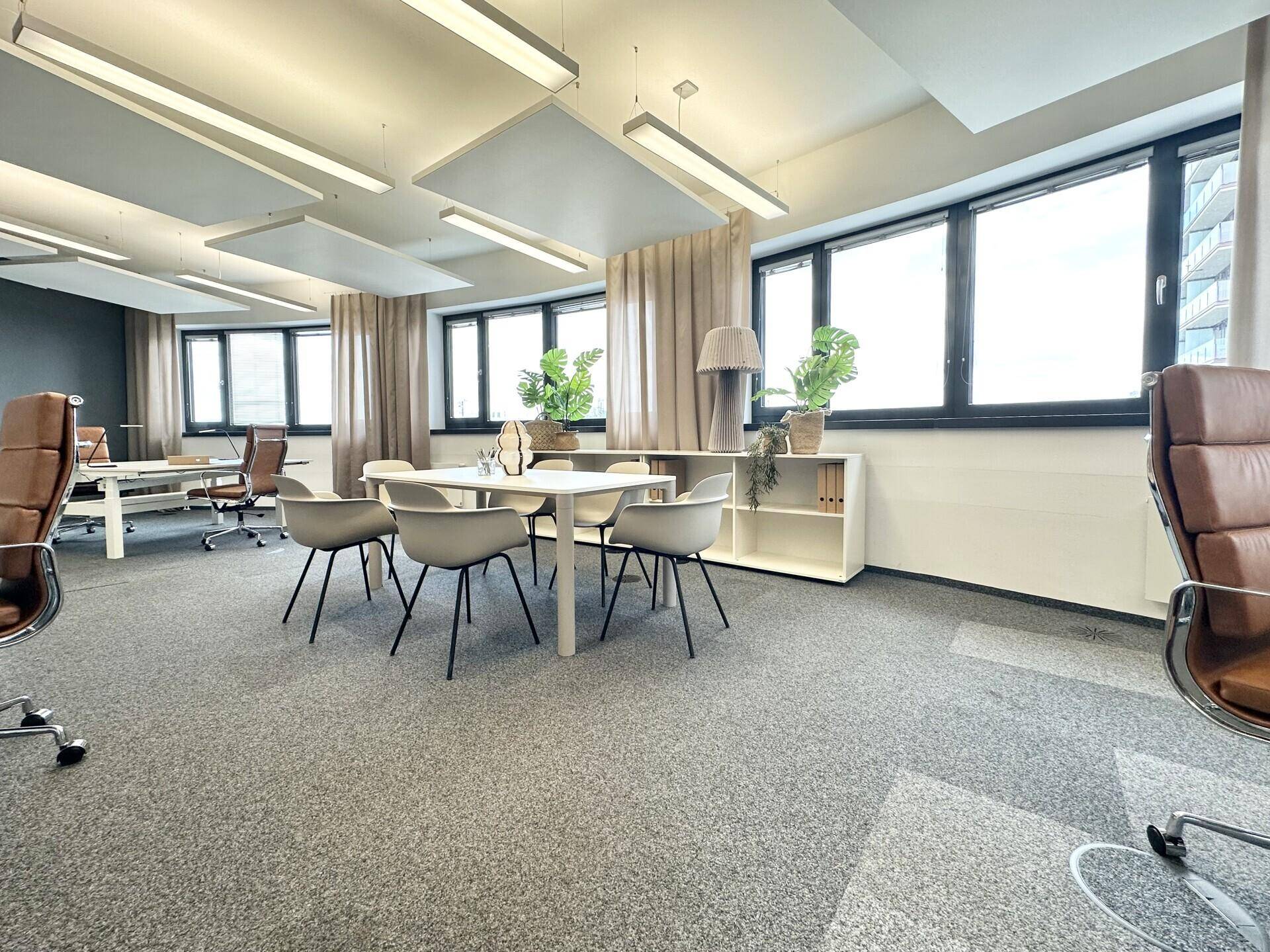 Offener Bürobereich mit mehreren Arbeitsplätzen und Besprechungstischen, hell und funktional eingerichtet.