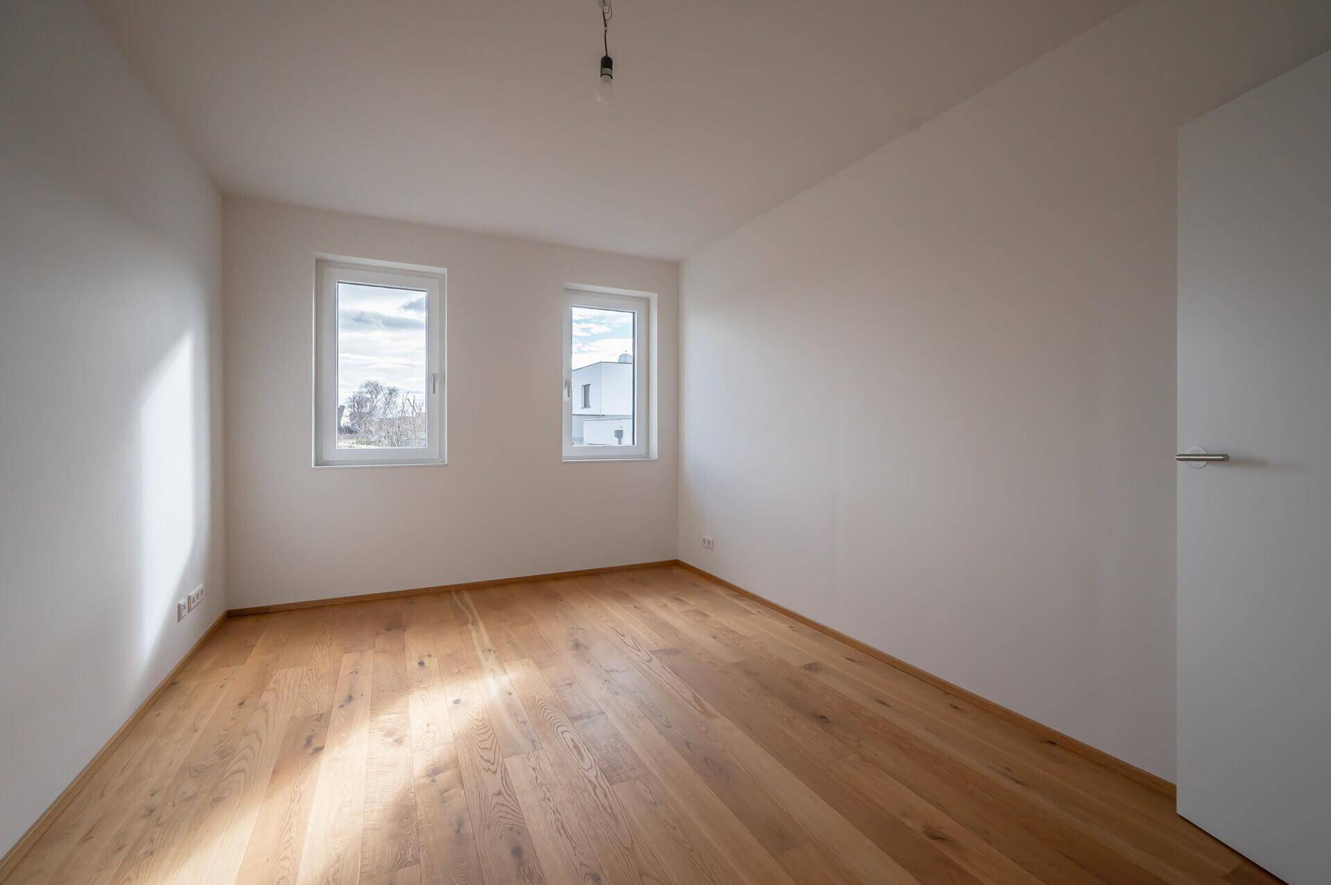 Helles Schlafzimmer mit Holzboden und zwei Fenstern.