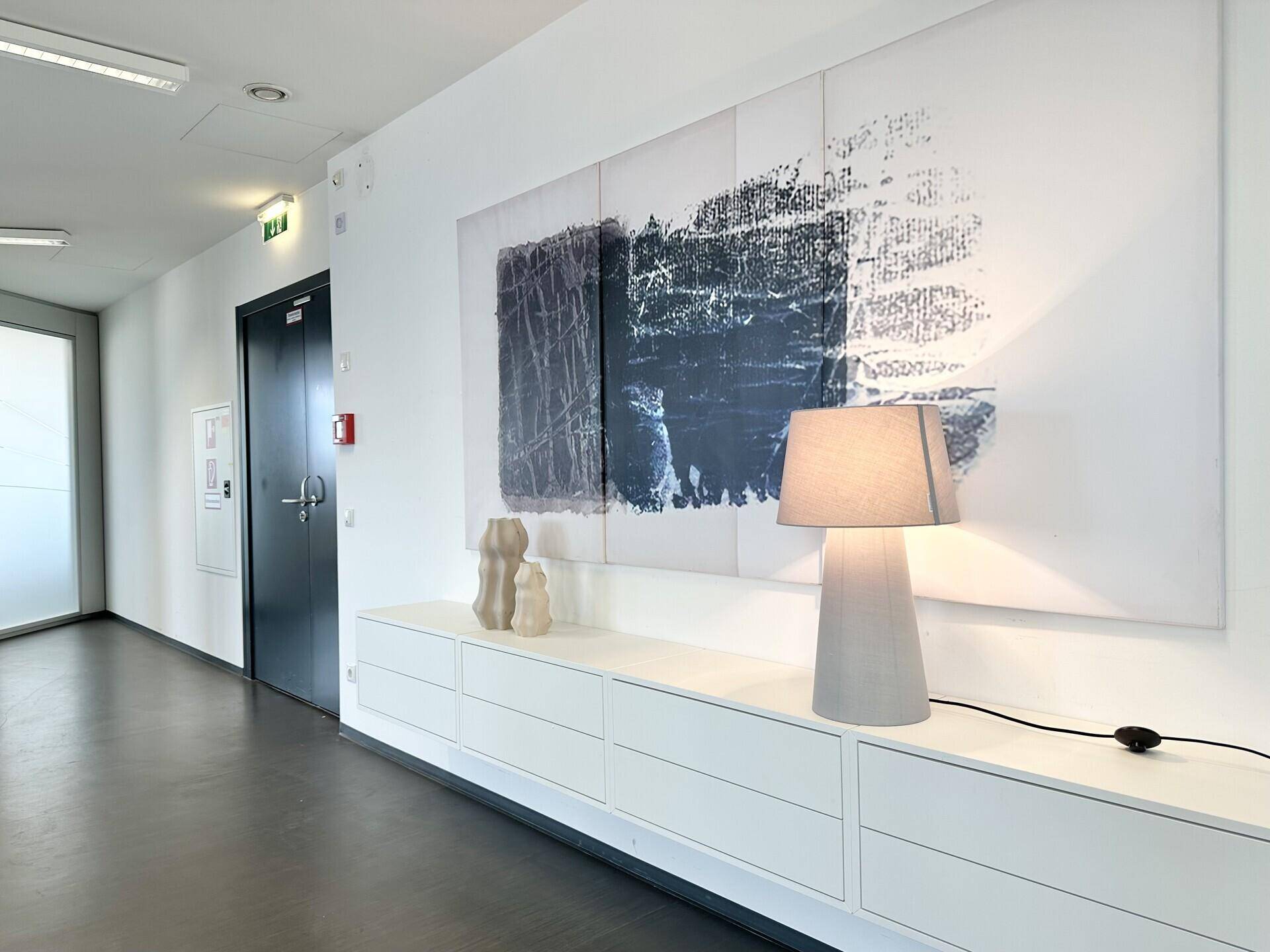 Heller Flur mit moderner Kunst an der Wand, weißem Sideboard und einer stilvollen Tischlampe.