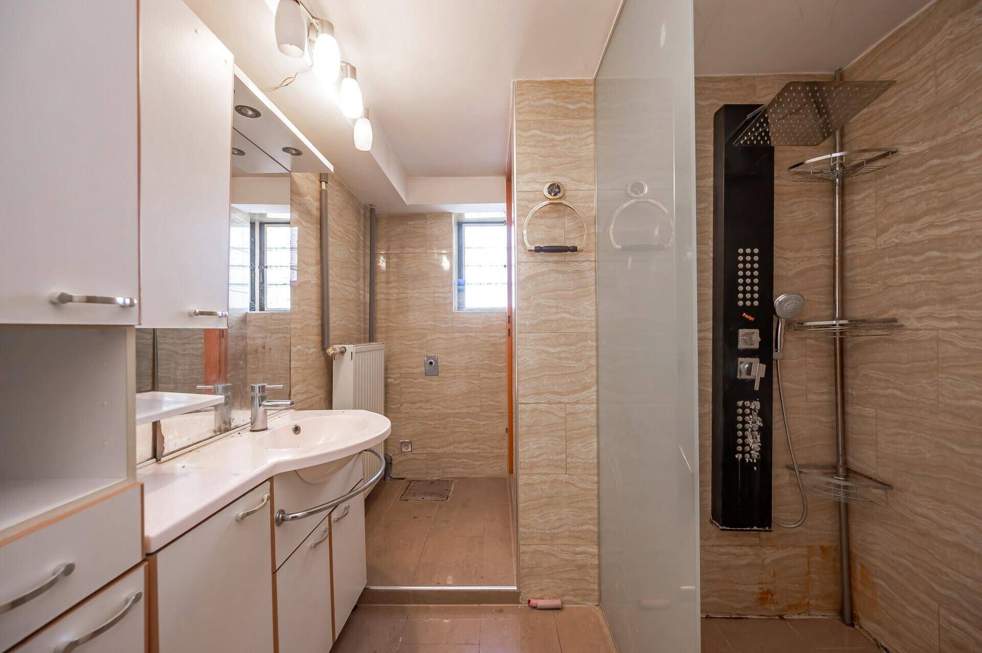 Modernes Badezimmer mit Duschkabine, Waschtisch und beigefarbenen Fliesen.