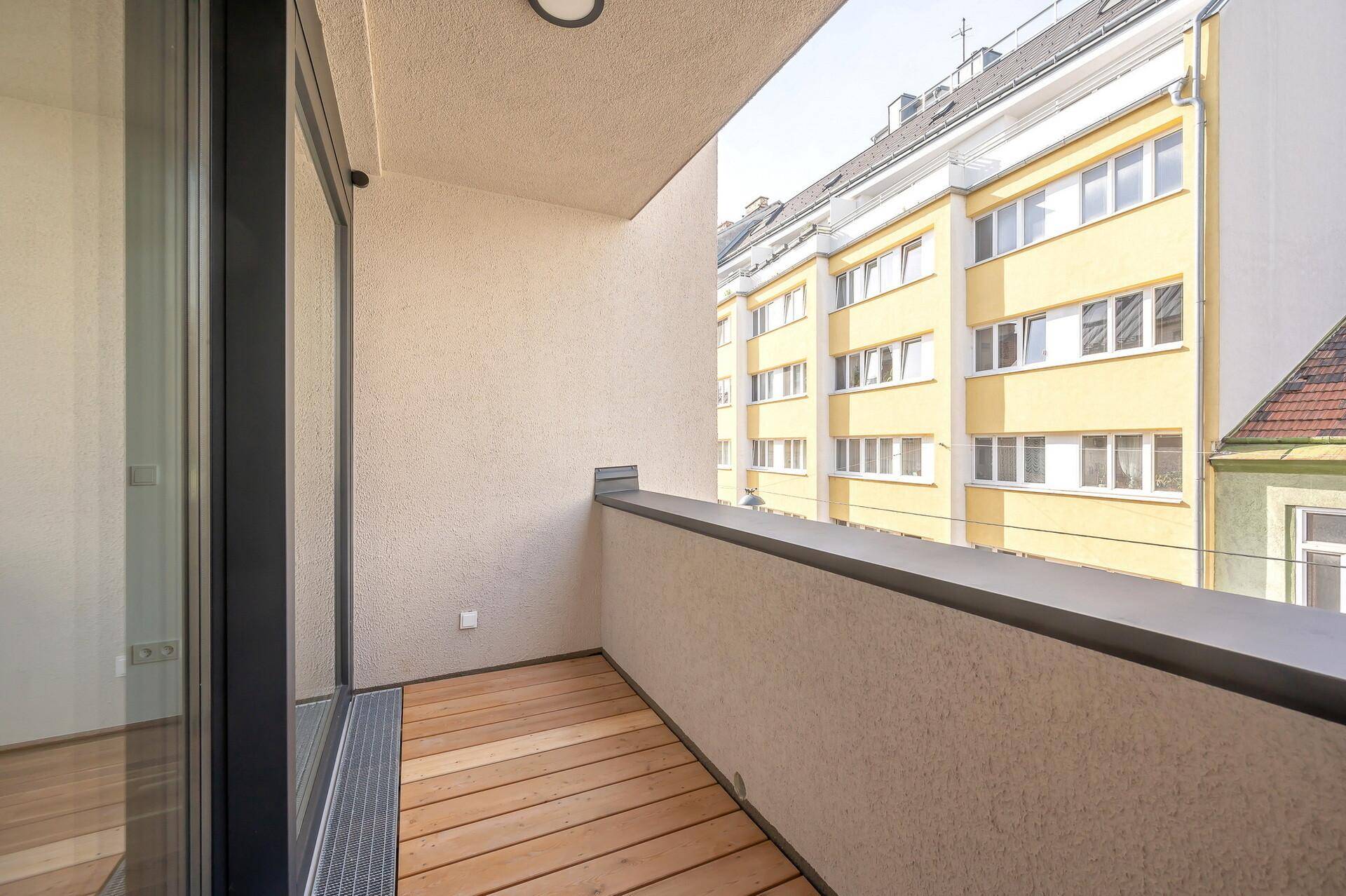 Moderner Balkon mit Holzboden und Blick auf die umliegenden Gebäude der Stadt.