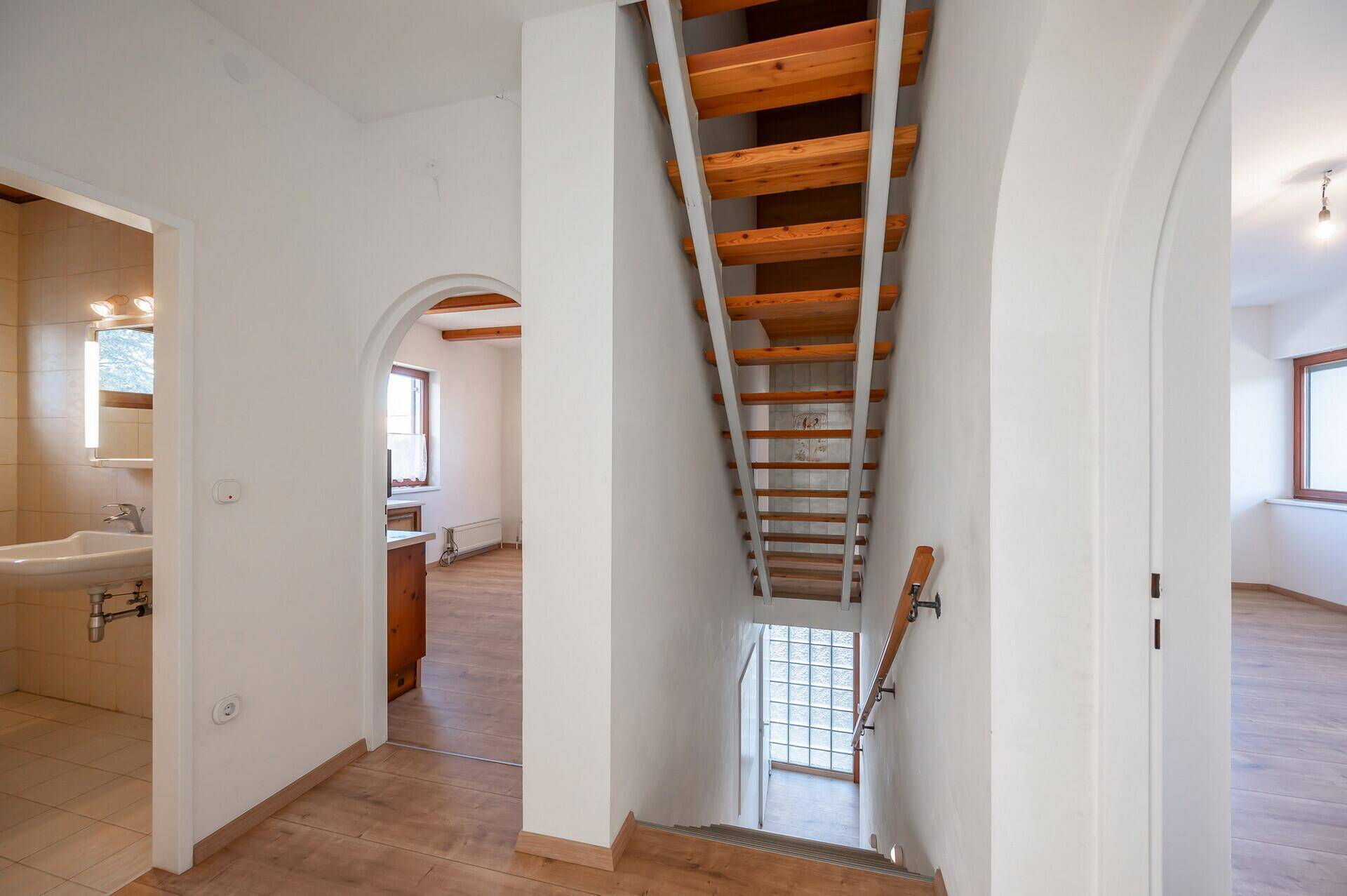 Geräumiger Flur mit offener Holztreppe und Rundbögen, die zu weiteren Räumen führen.