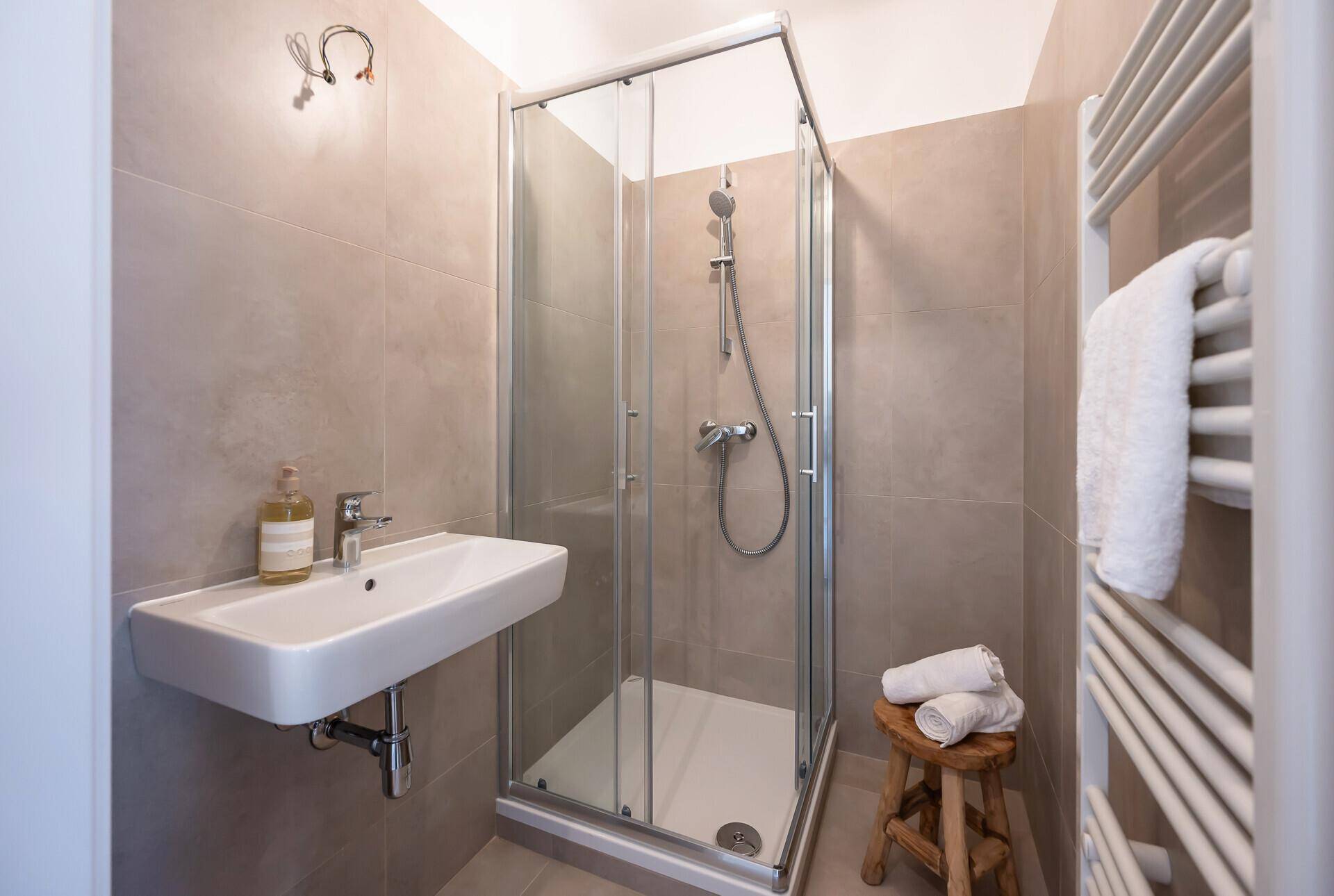 Modernes Badezimmer mit Duschkabine, Waschbecken und beheiztem Handtuchhalter.