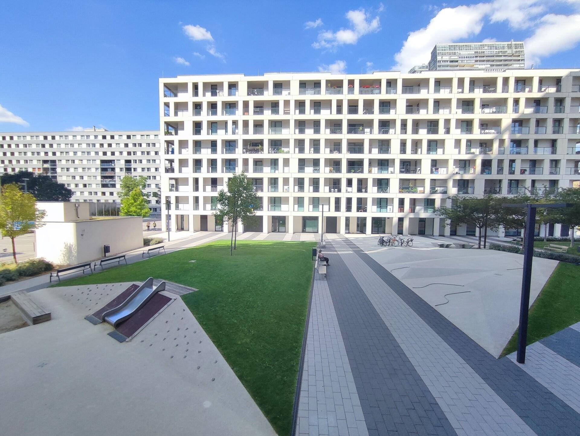 Weitläufige Wohnanlage mit Grünflächen und Spielplatz, umgeben von modernen Gebäuden.