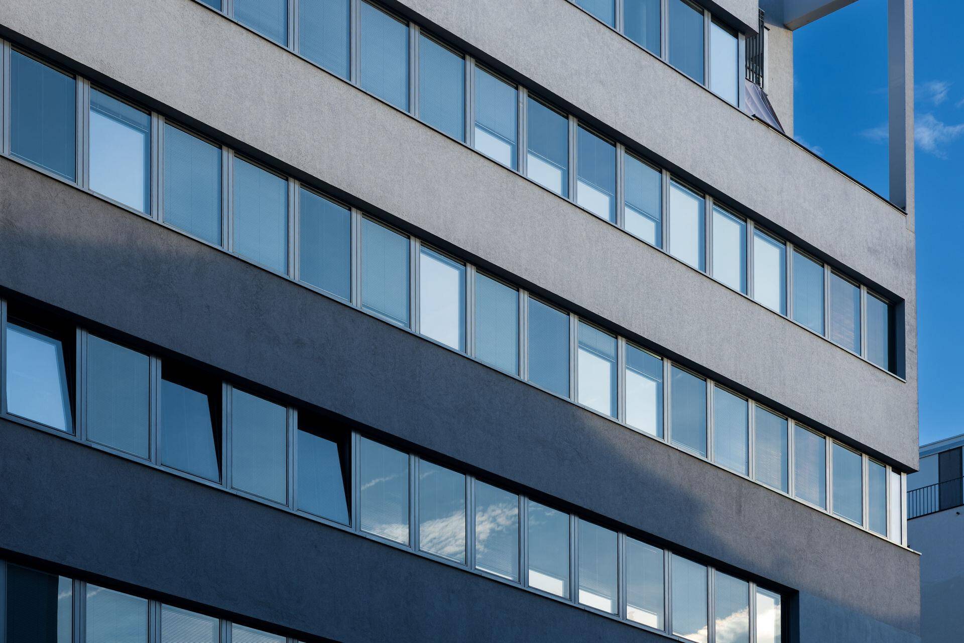 Nahaufnahme der modernen Fassade mit vielen Fenstern, die den Himmel widerspiegeln.