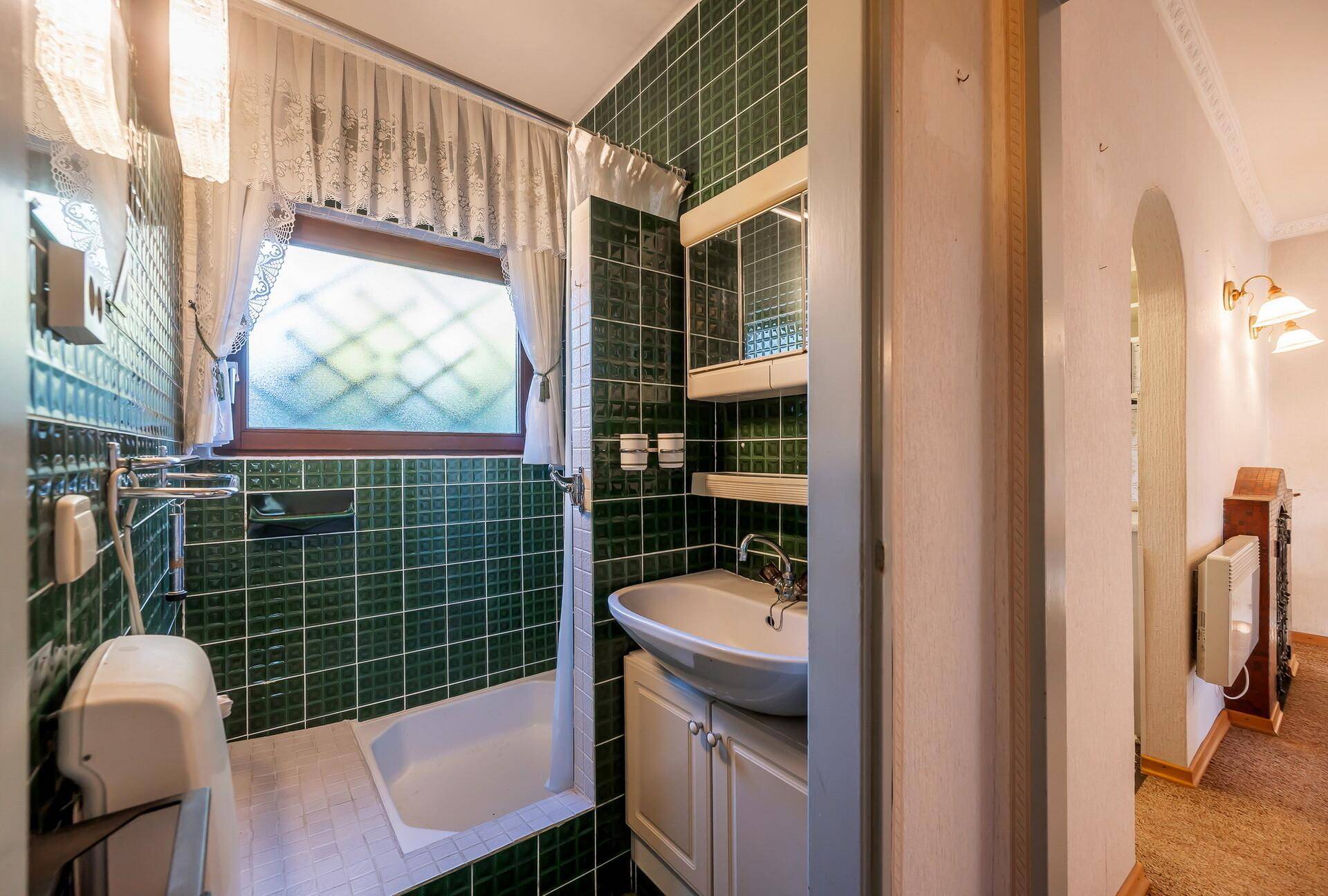 Badezimmer mit grünen Fliesen, Waschbecken und Badewanne, ausgestattet mit einem Fenster.