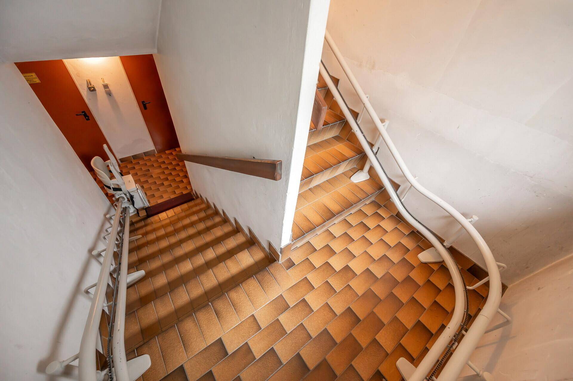 Treppenhaus mit Fliesenboden und Handlauf, das in den unteren Bereich führt.