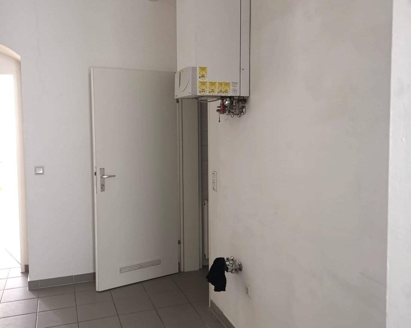 Wandmontierter Heizkessel in einem gefliesten Bereich, möglicherweise ein Hauswirtschaftsraum.