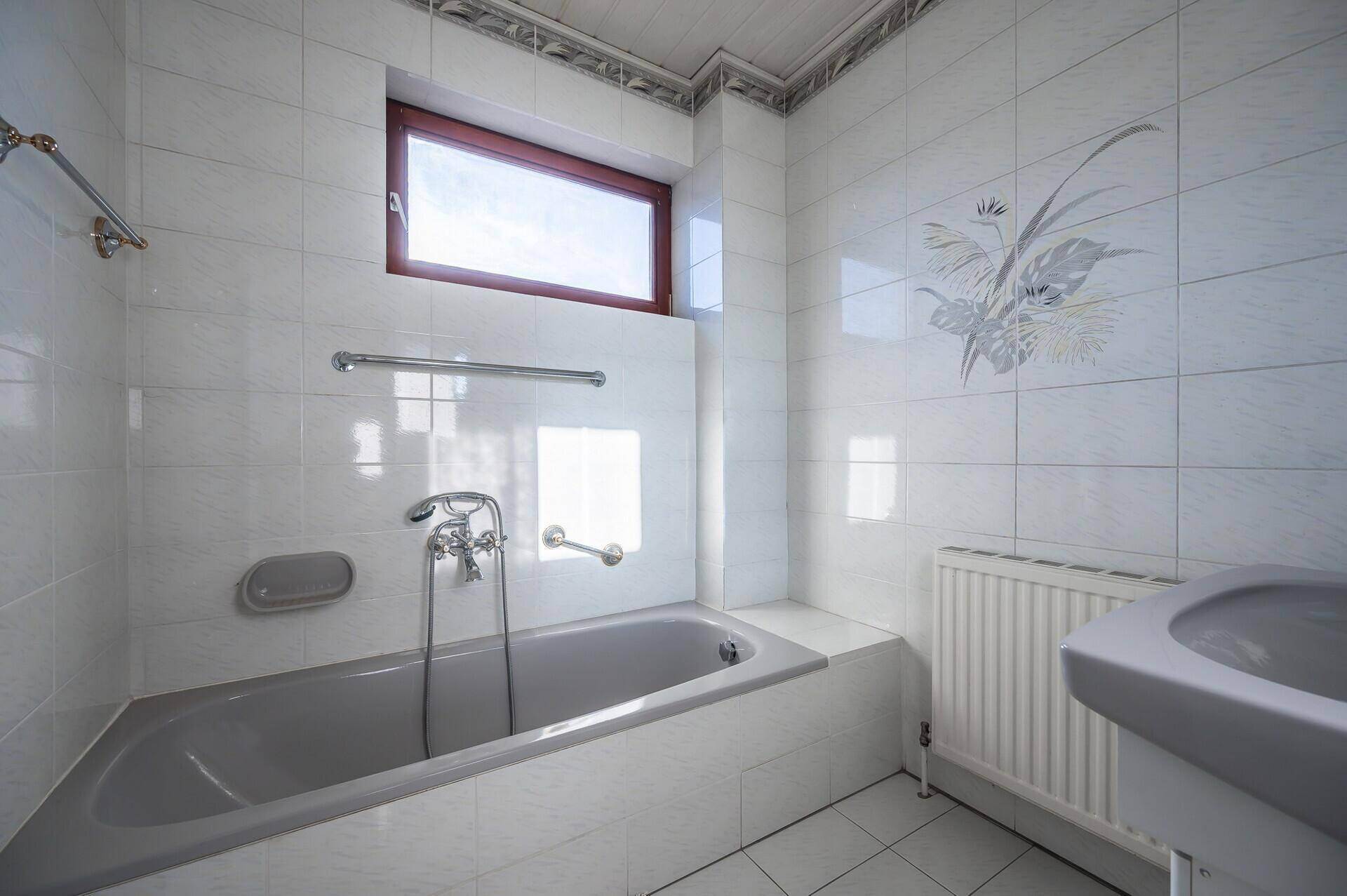 Detailansicht der Badewanne mit Armaturen, Haltegriffen und dekorativen Fliesen.