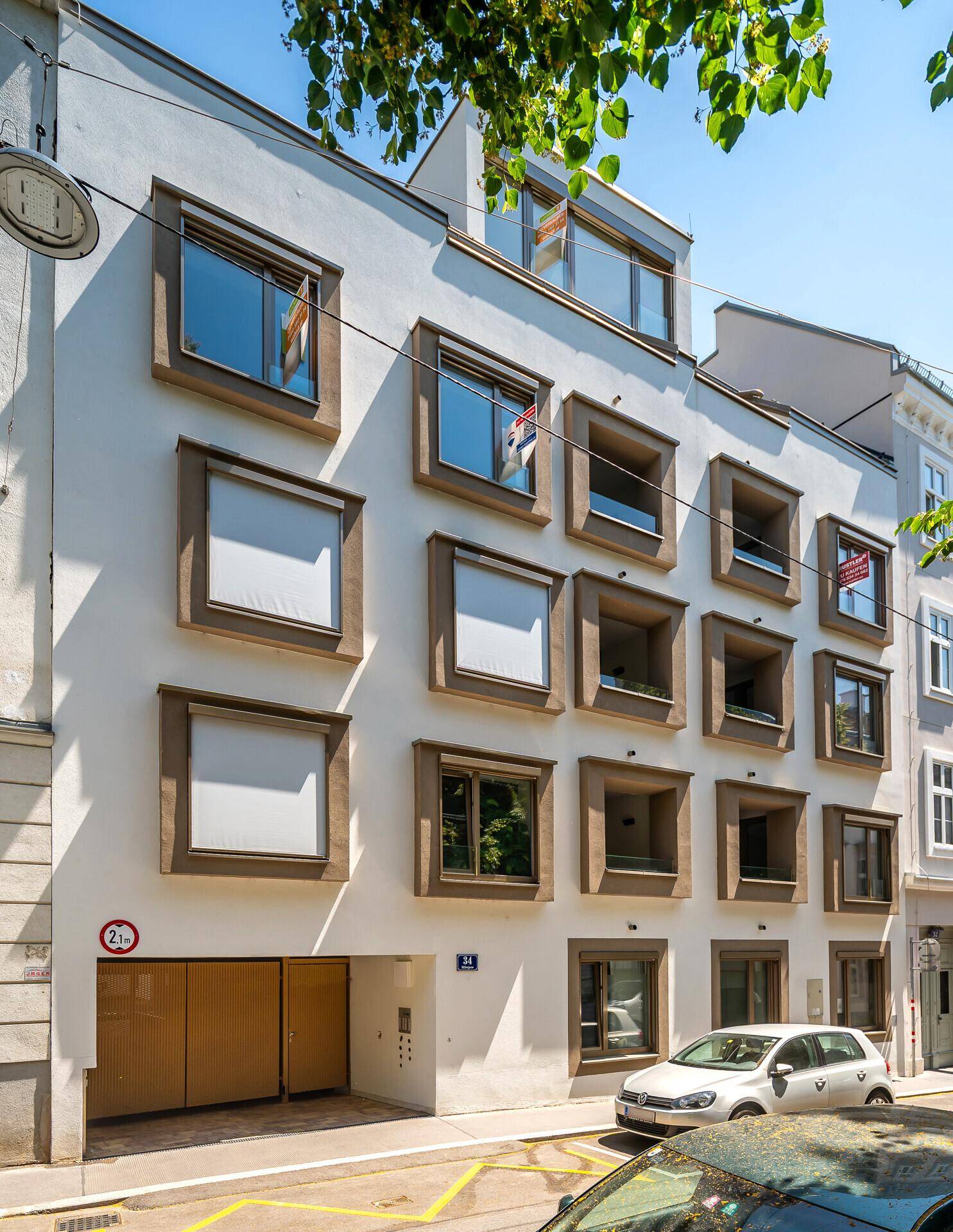 Zeitgenössische Gebäudefassade mit markanten Fensterrahmen und Tiefgaragenzugang an sonnigem Tag.