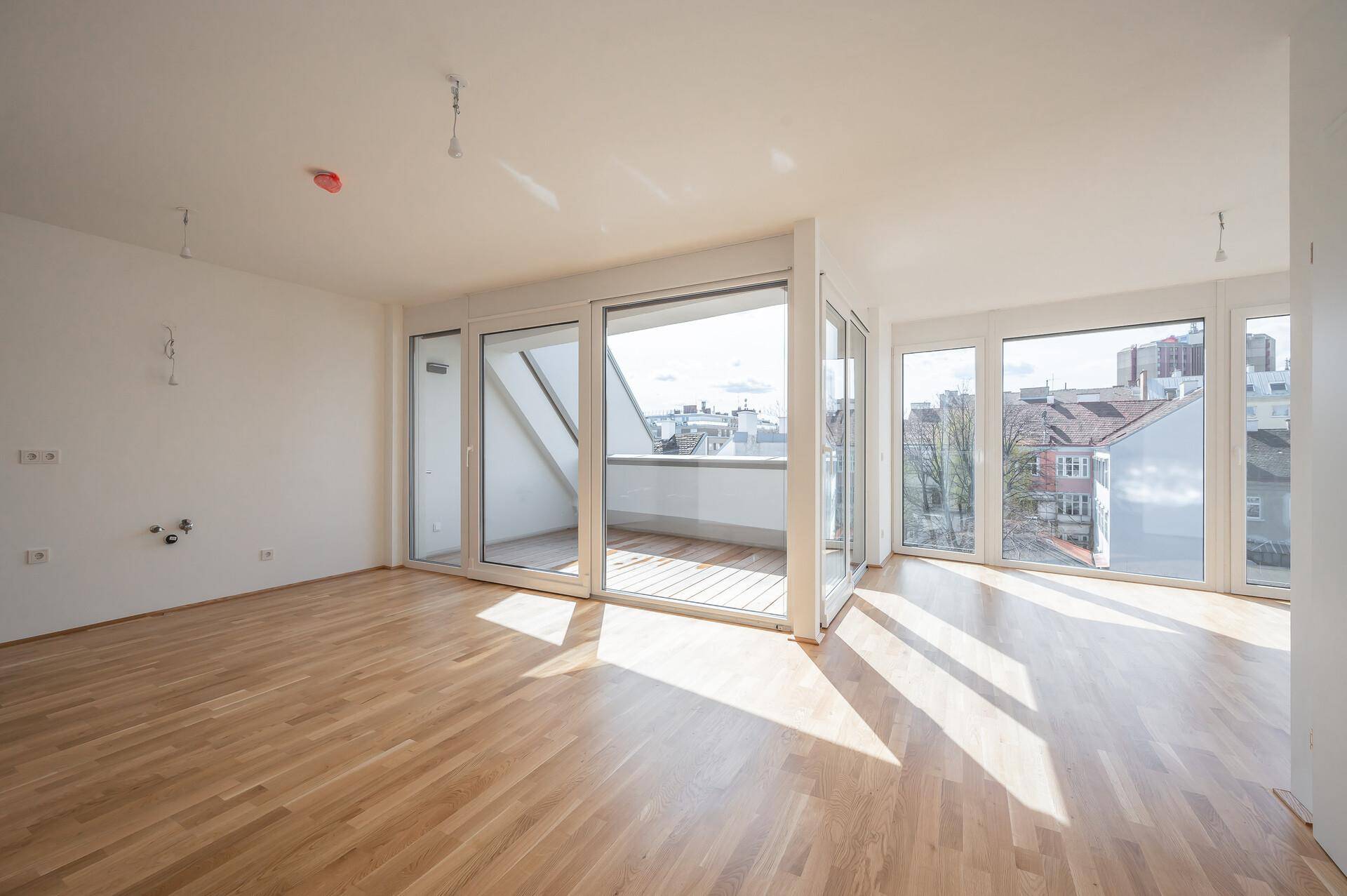 Geräumiger Wohnbereich mit Holzboden, weißen Wänden und direktem Zugang zu einem sonnigen Balkon.