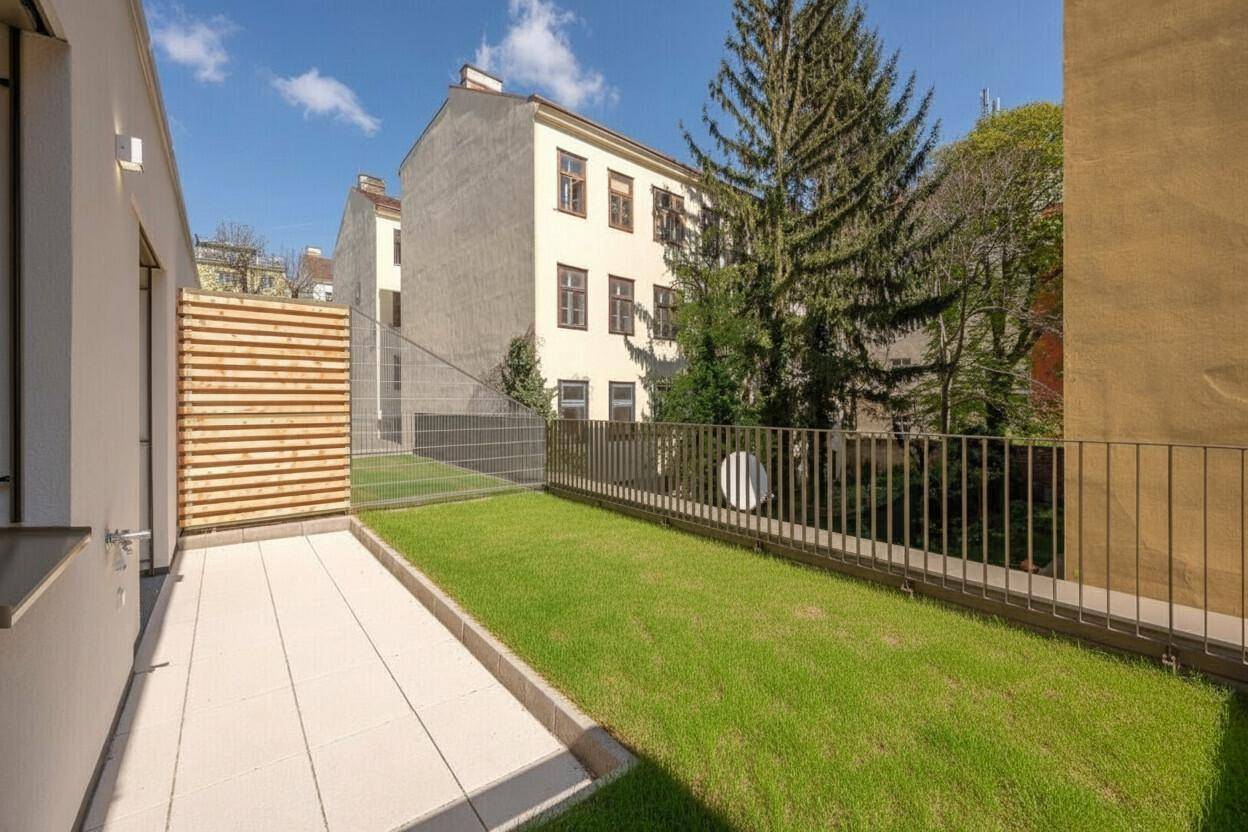 Gepflegter Gartenbereich mit Rasenfläche und Terrasse, umgeben von einem Zaun und Bäumen.