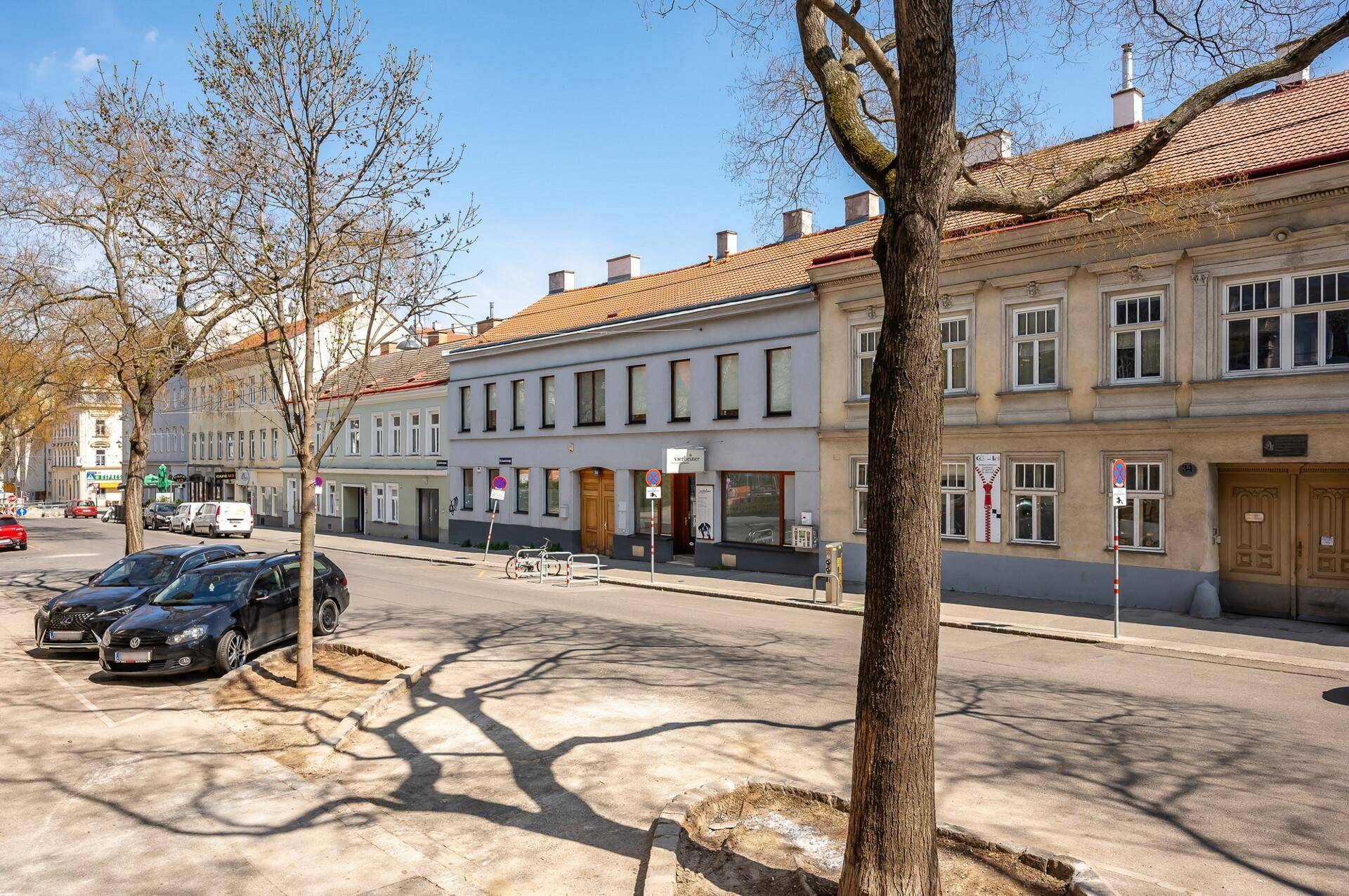 Blick auf eine belebte Straße mit parkenden Autos und historischen Gebäuden unter blauem Himmel.