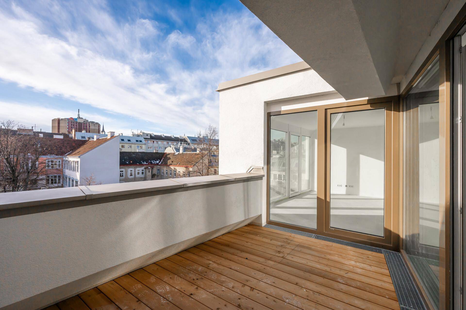 Geräumiger Balkon mit Holzboden und Stadtblick unter blauem Himmel.