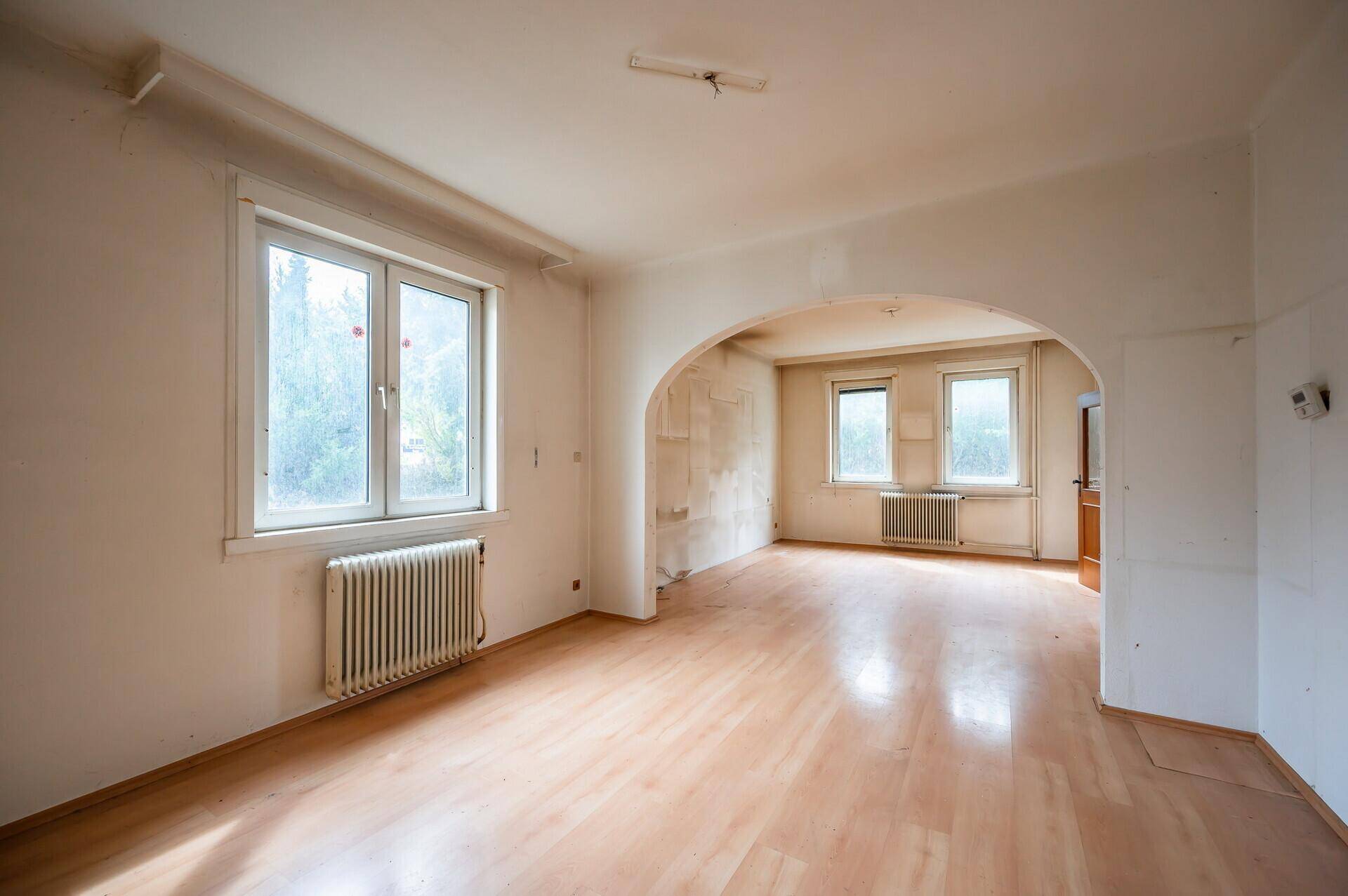 Heller Wohnraum mit Holzboden und Rundbogen, der zu einem weiteren Zimmer führt.