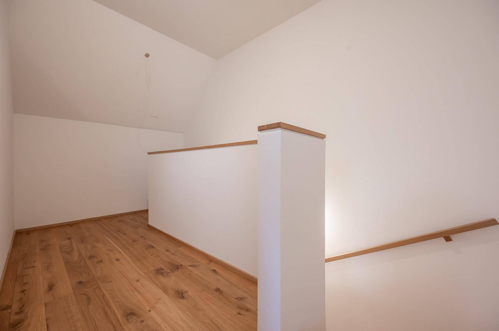 Heller Flurbereich im Obergeschoss mit Holzfußboden und Dachschräge, offen und einladend.