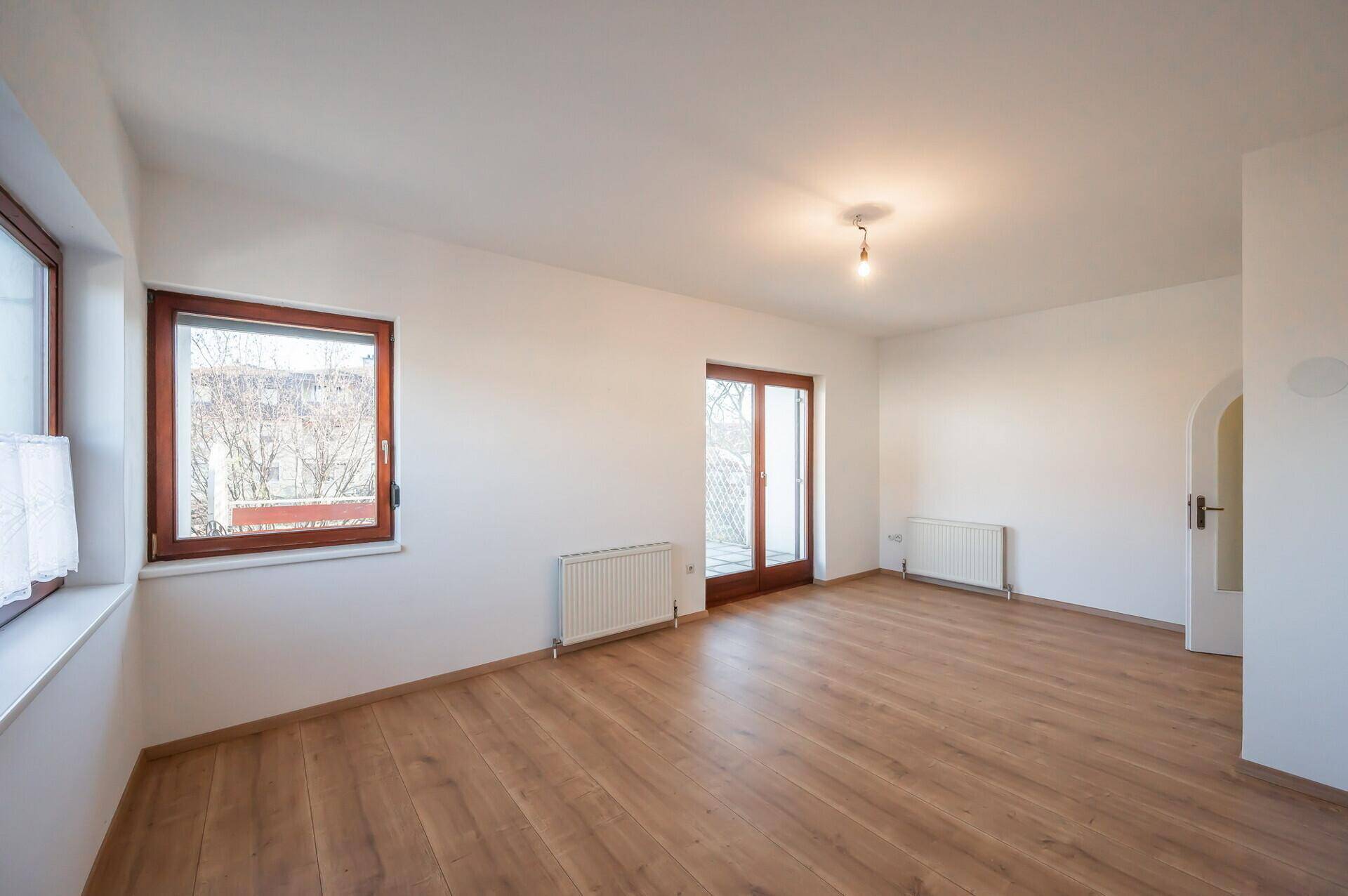 Helles Wohnzimmer mit Holzboden, weißen Wänden und einem Fenster mit Blick nach draußen.